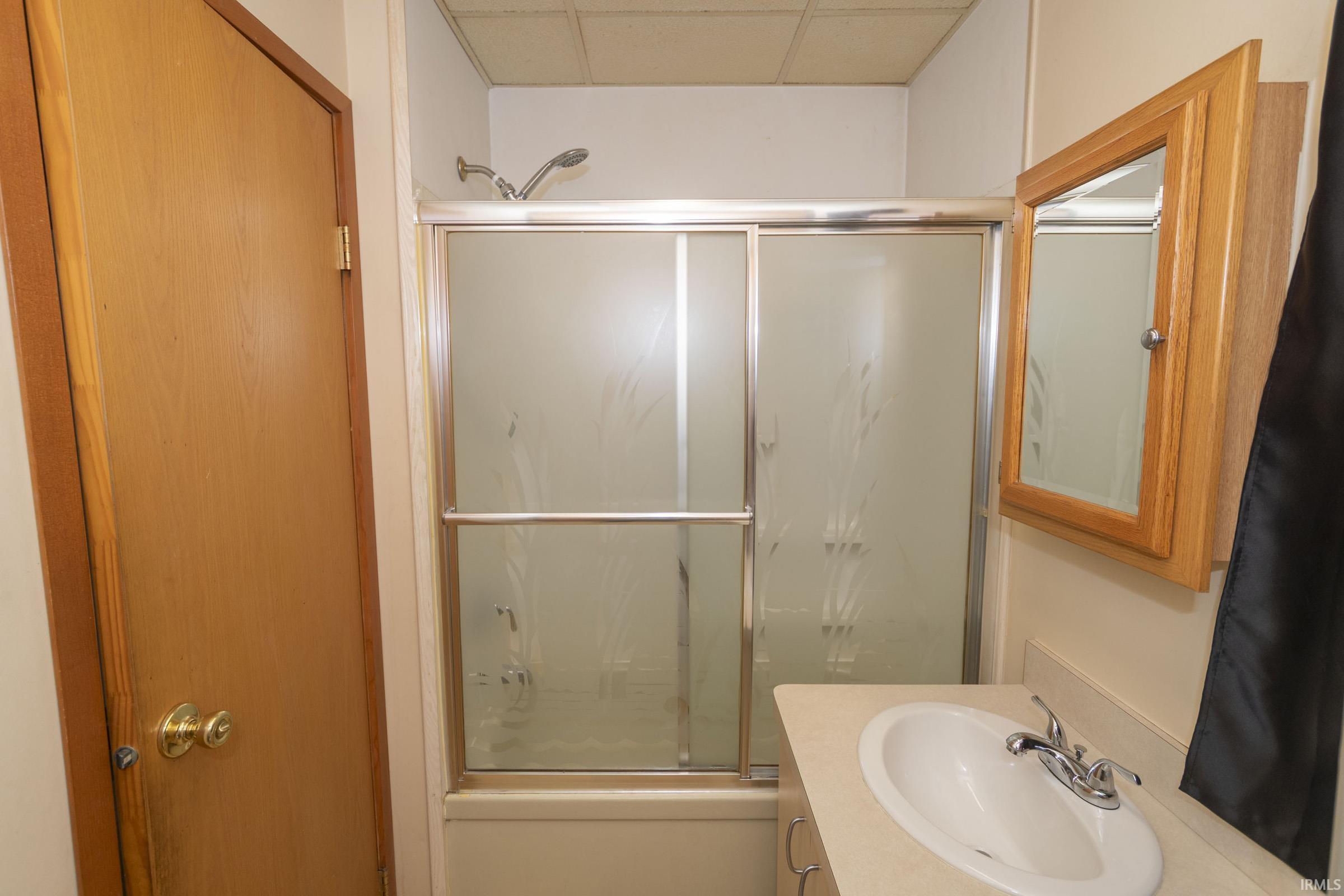 Bathroom featuring a shower with sliding frosted glass doors, a vanity with an integrated sink, a wall-mounted medicine cabinet with a wood-finish frame, and a chrome faucet