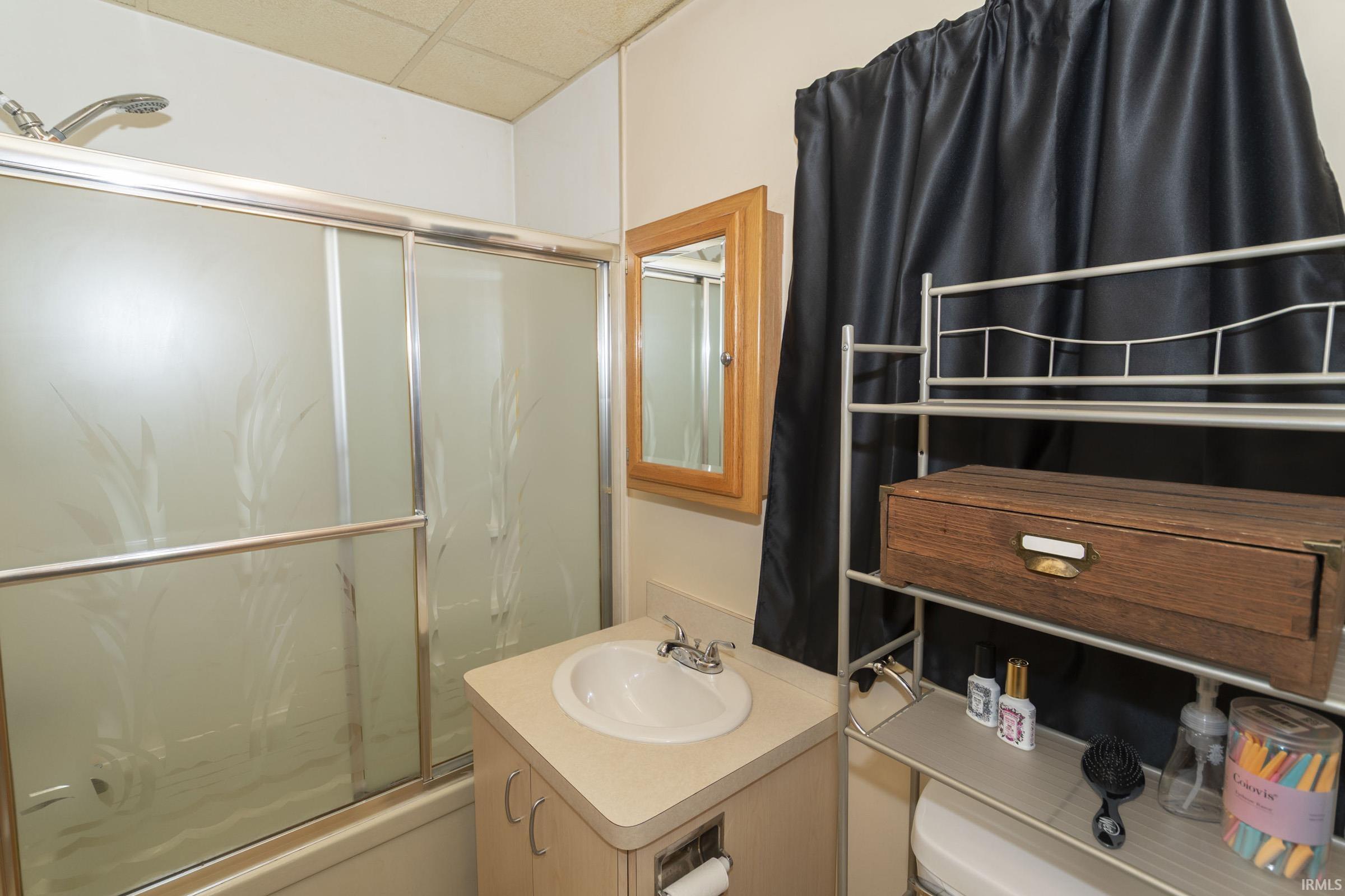 Bathroom featuring a shower-tub combination with frosted sliding glass doors, a single vanity with an integrated sink, a medicine cabinet with a wood-finish frame, and overhead storage shelving