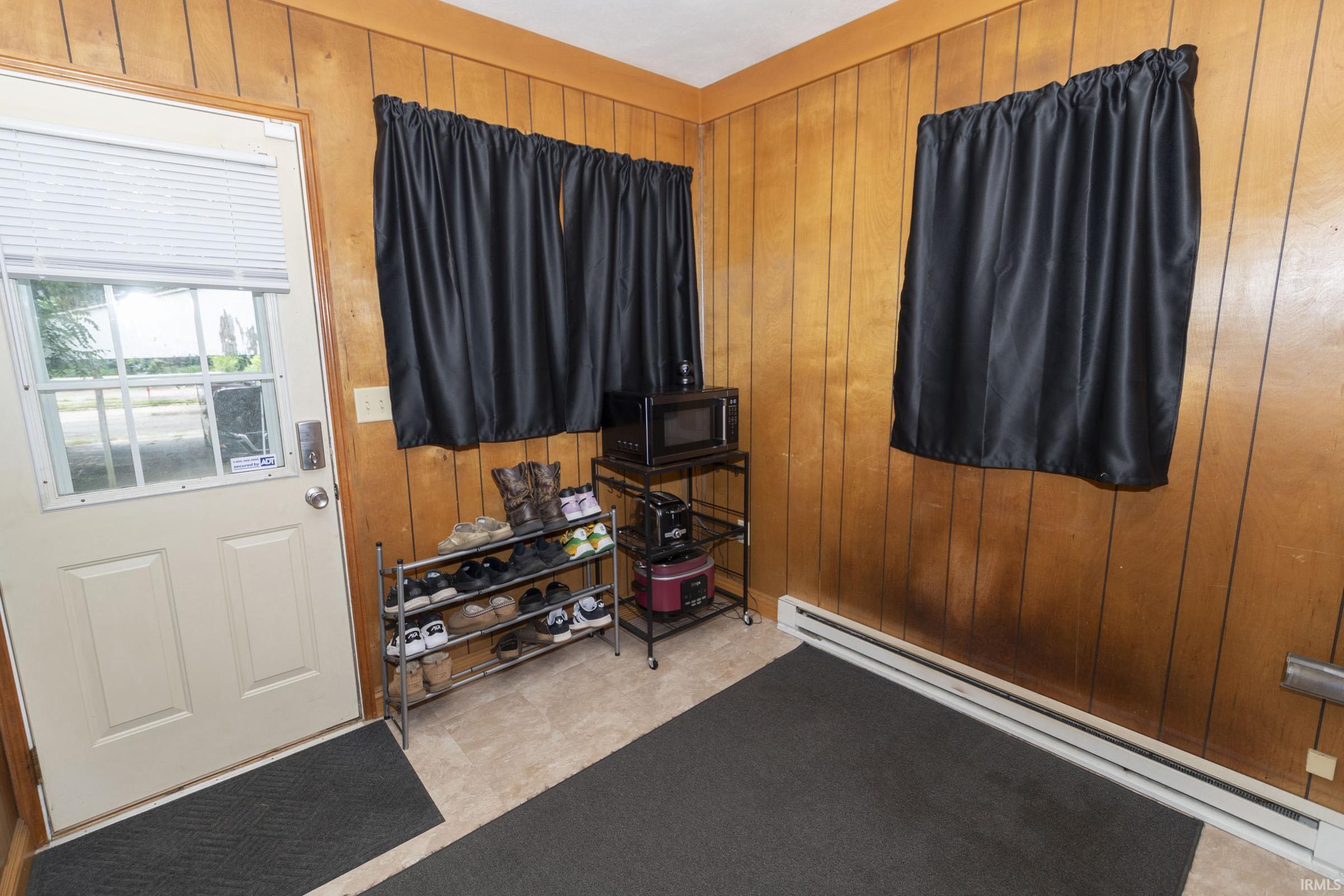 Entryway featuring paneled wood-finish walls, light-toned flooring, an exterior door with integrated window blinds, and baseboard heating