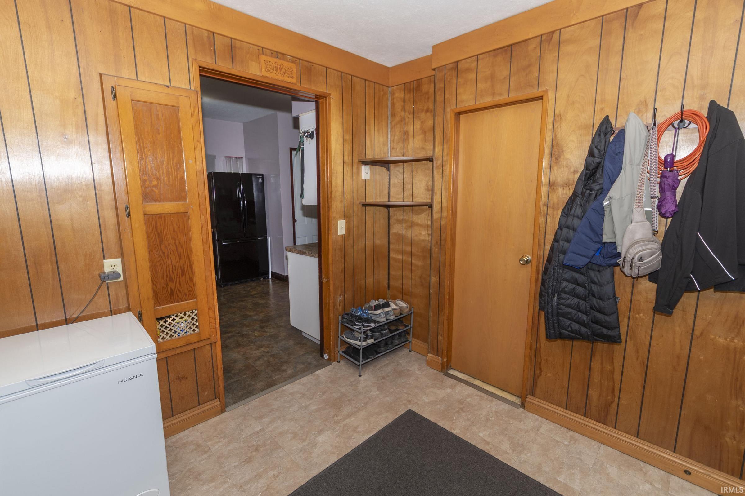 Wood-paneled room featuring light-toned flooring and an open doorway to an interior space
