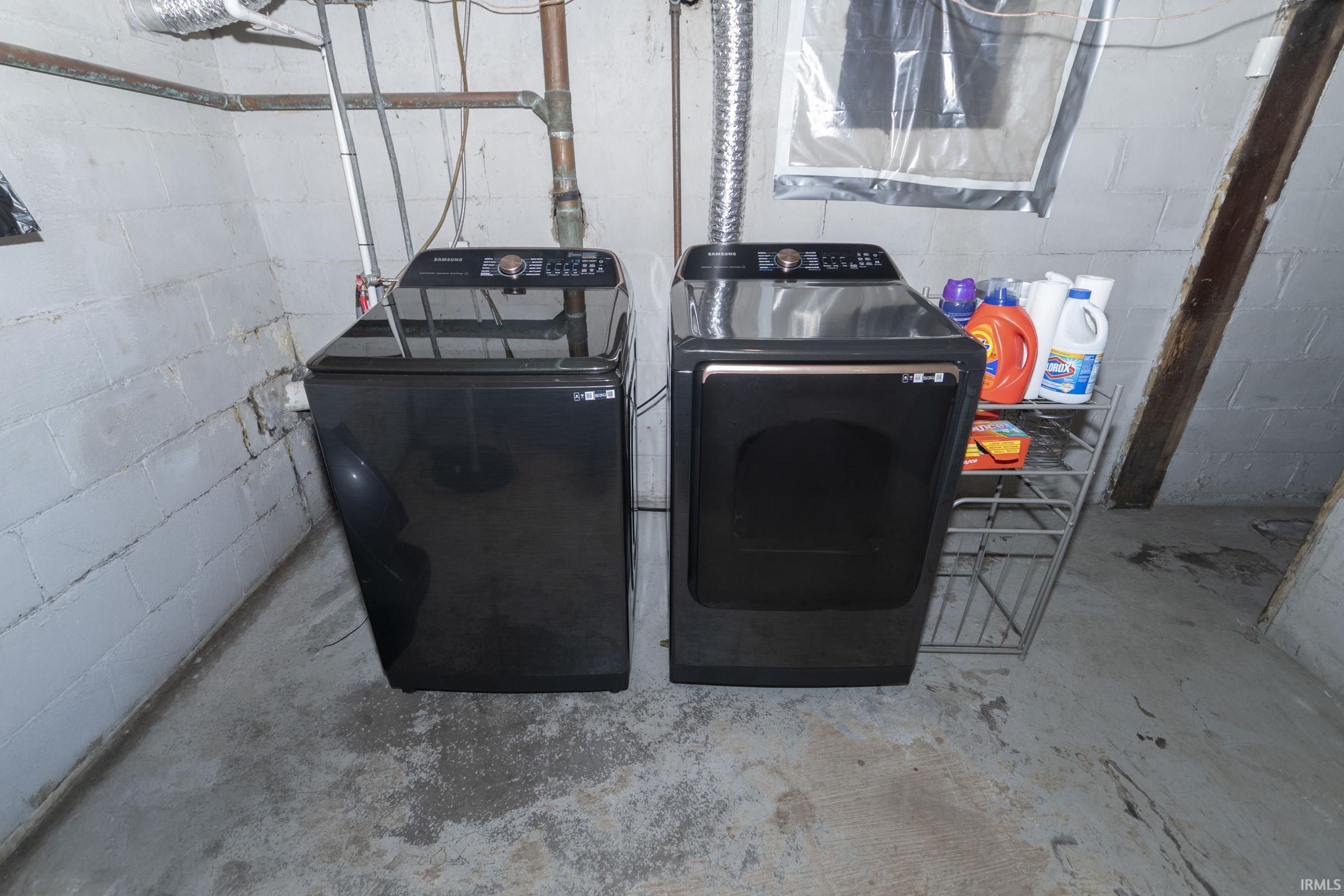 Laundry area featuring a top-load washing machine and front-load dryer set, exposed copper piping, and concrete block walls