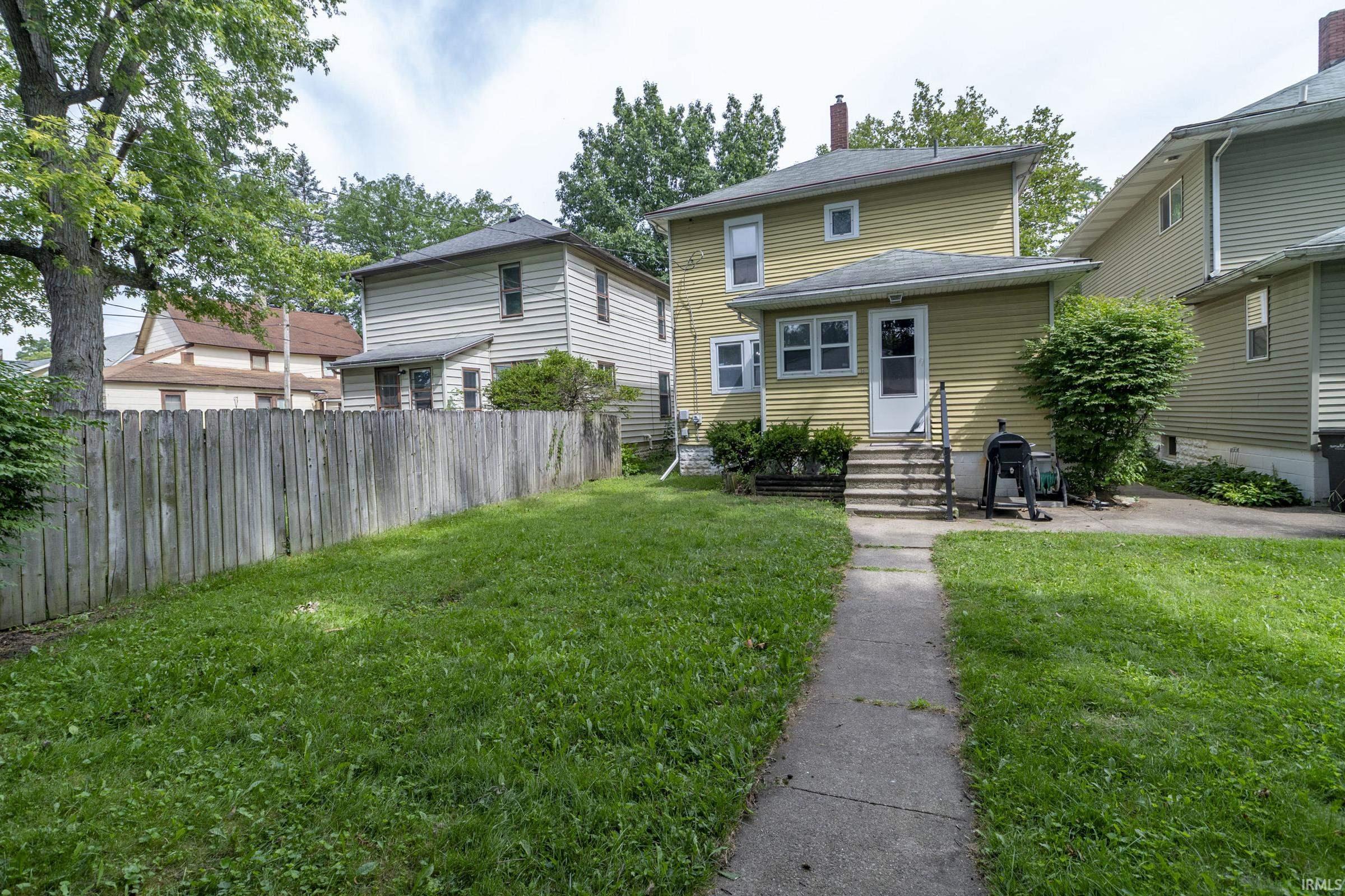 Expansive rear yard featuring green lawn, mature perimeter trees, and wood privacy fencing