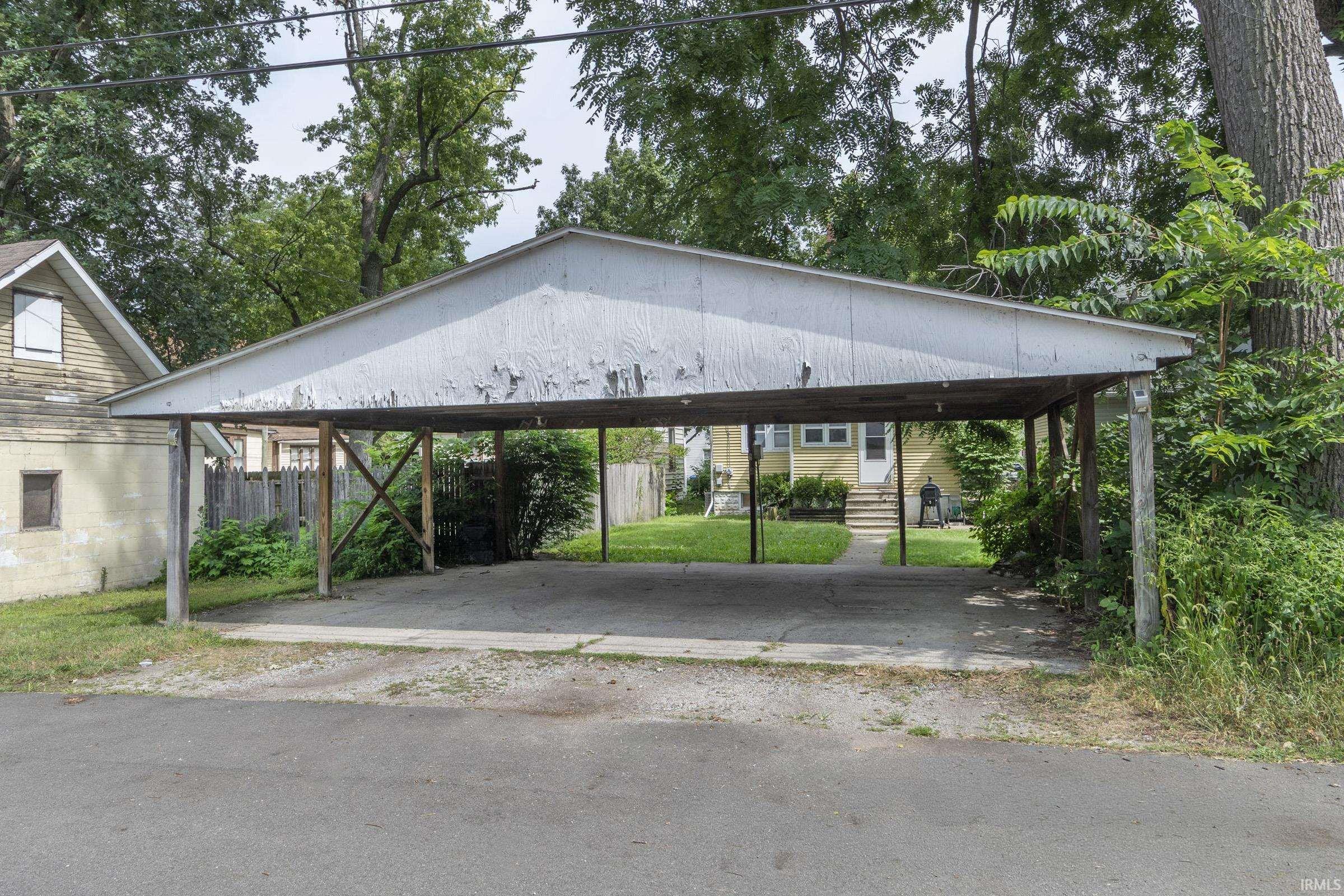 Open carport featuring a concrete parking pad, wood support beams, and a pitched roof