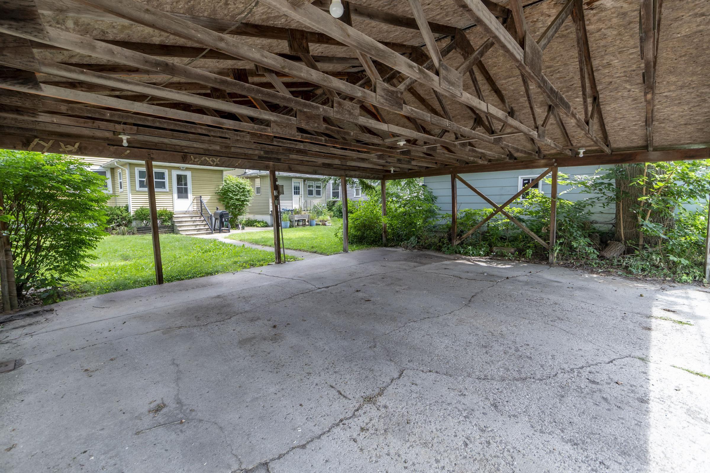 Carport with a concrete slab, exposed wood framing, and a wood-panel ceiling
