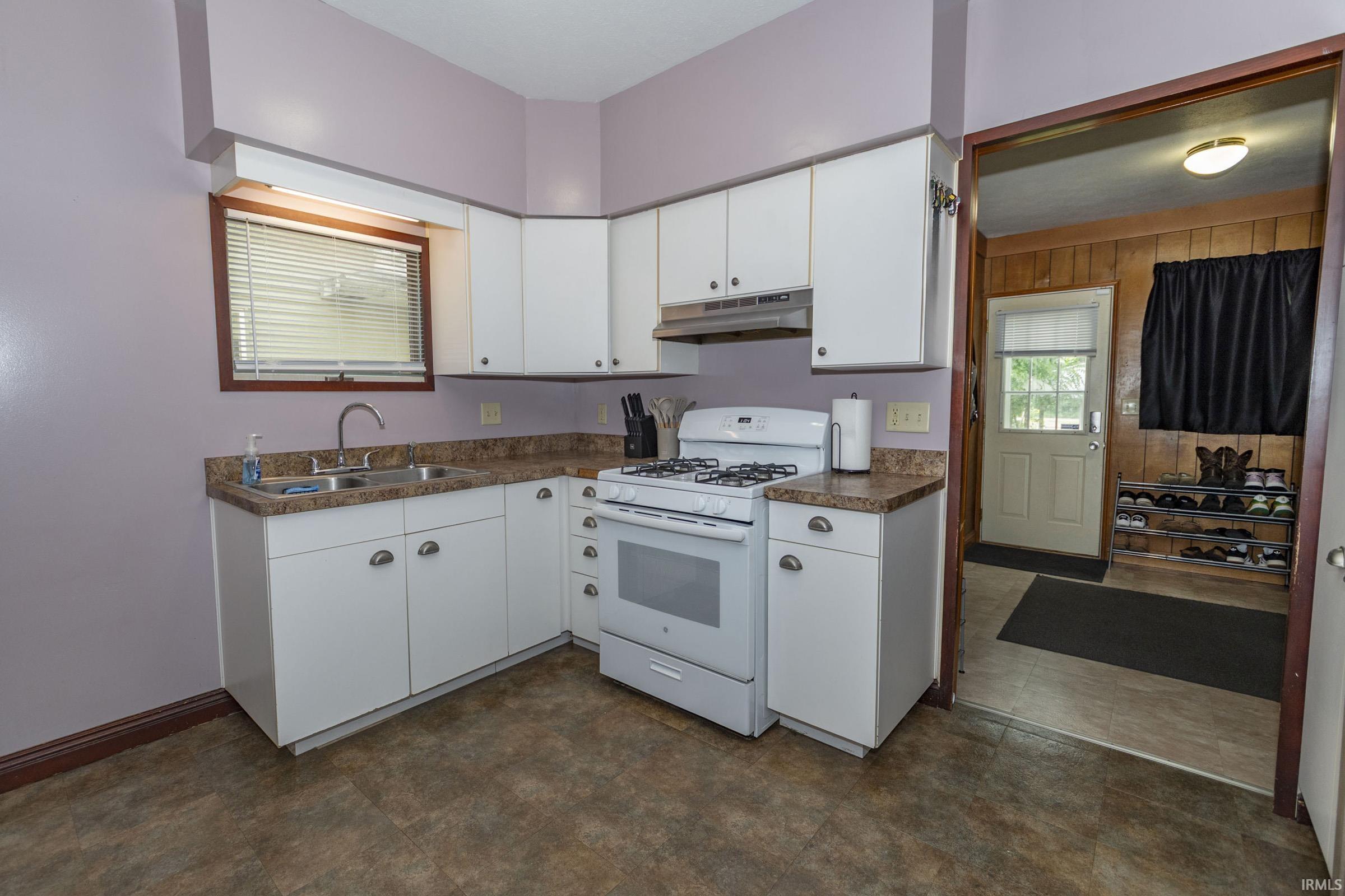 Kitchen featuring white cabinetry, a double basin stainless steel sink, a gas range, and laminate countertops