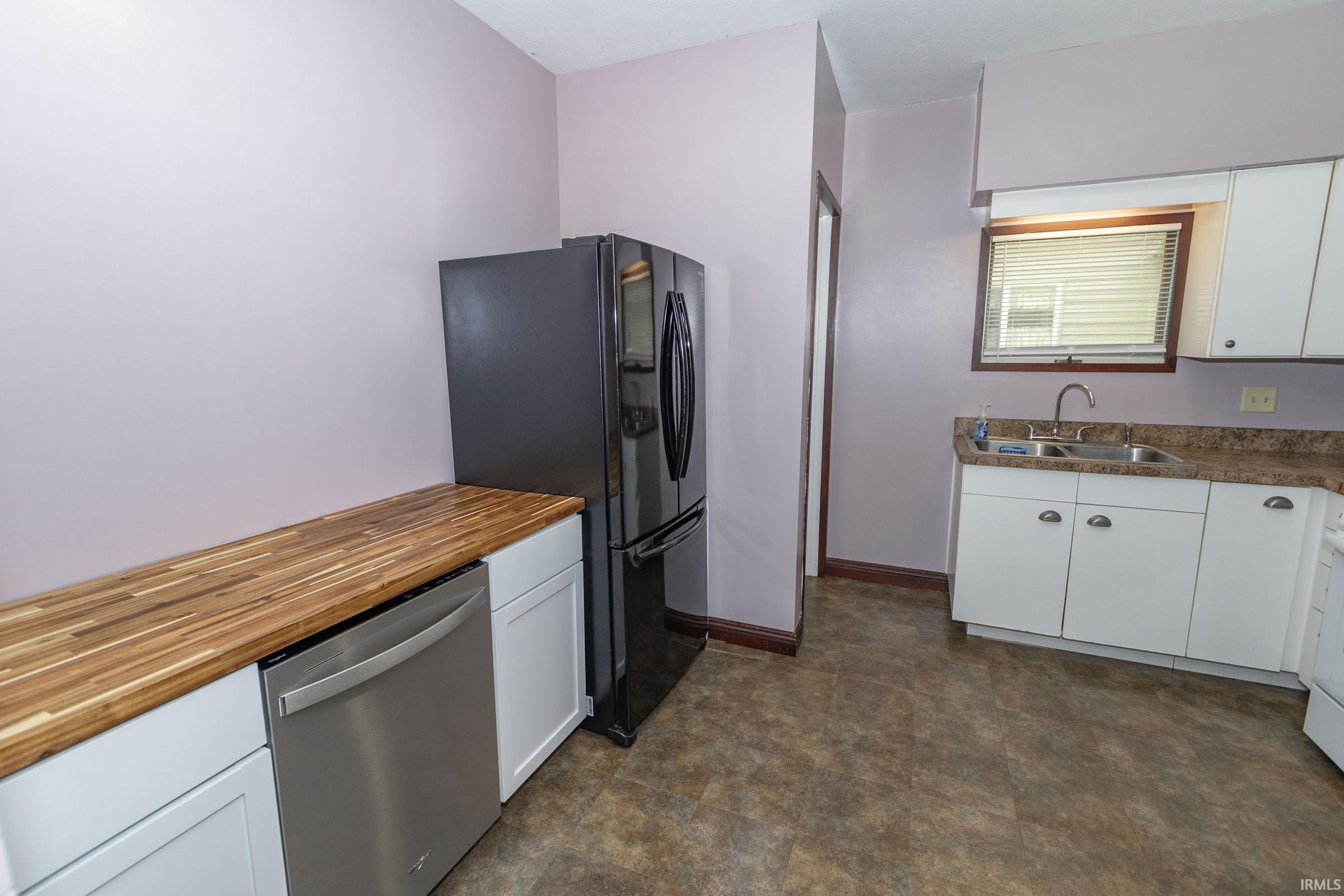 Kitchen featuring a stainless steel dishwasher, modern black refrigerator, butcher block style countertops, white cabinetry, and a double basin sink