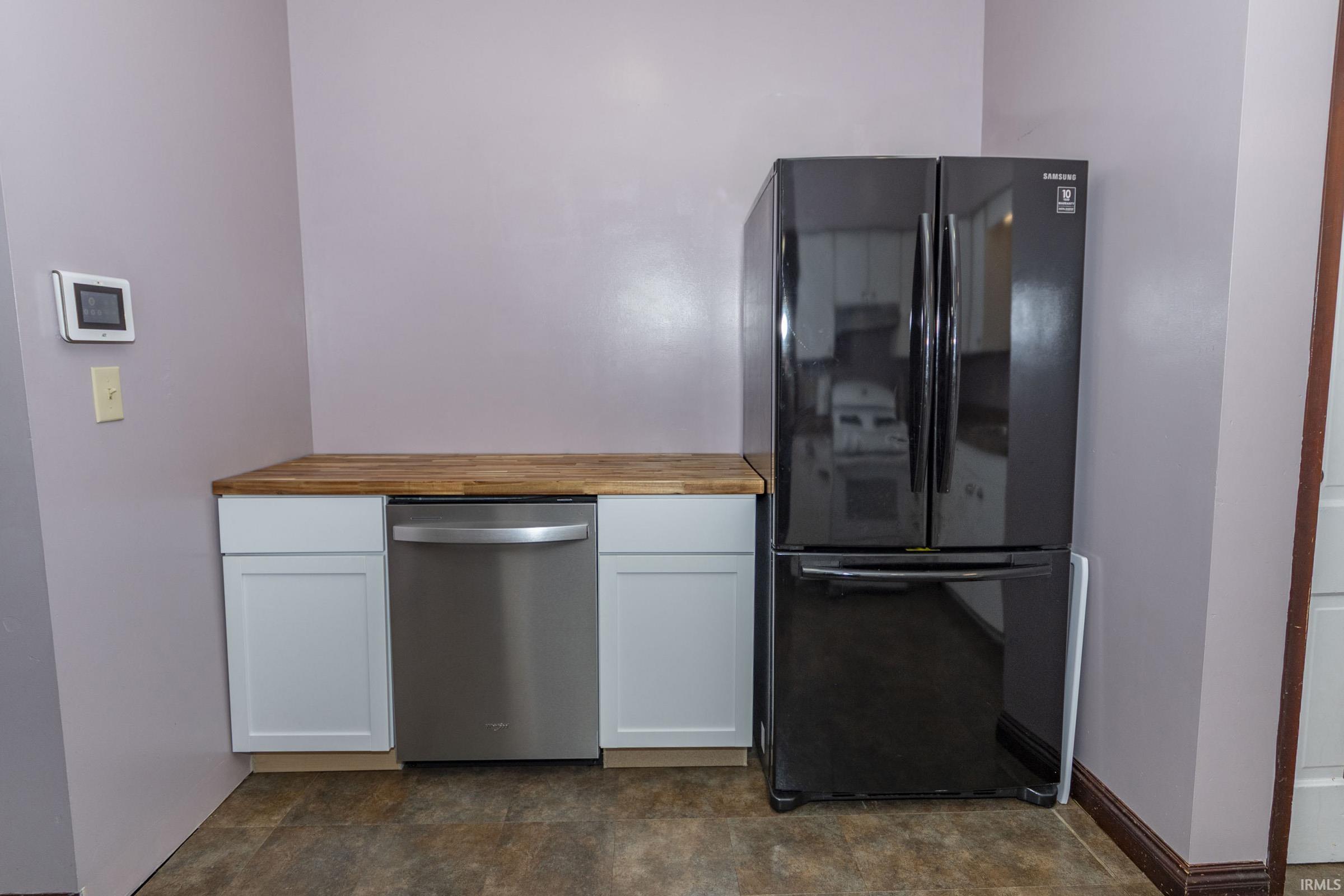 Kitchenette area featuring a wood-finish countertop, white base cabinetry, a stainless steel dishwasher, and a black French door refrigerator