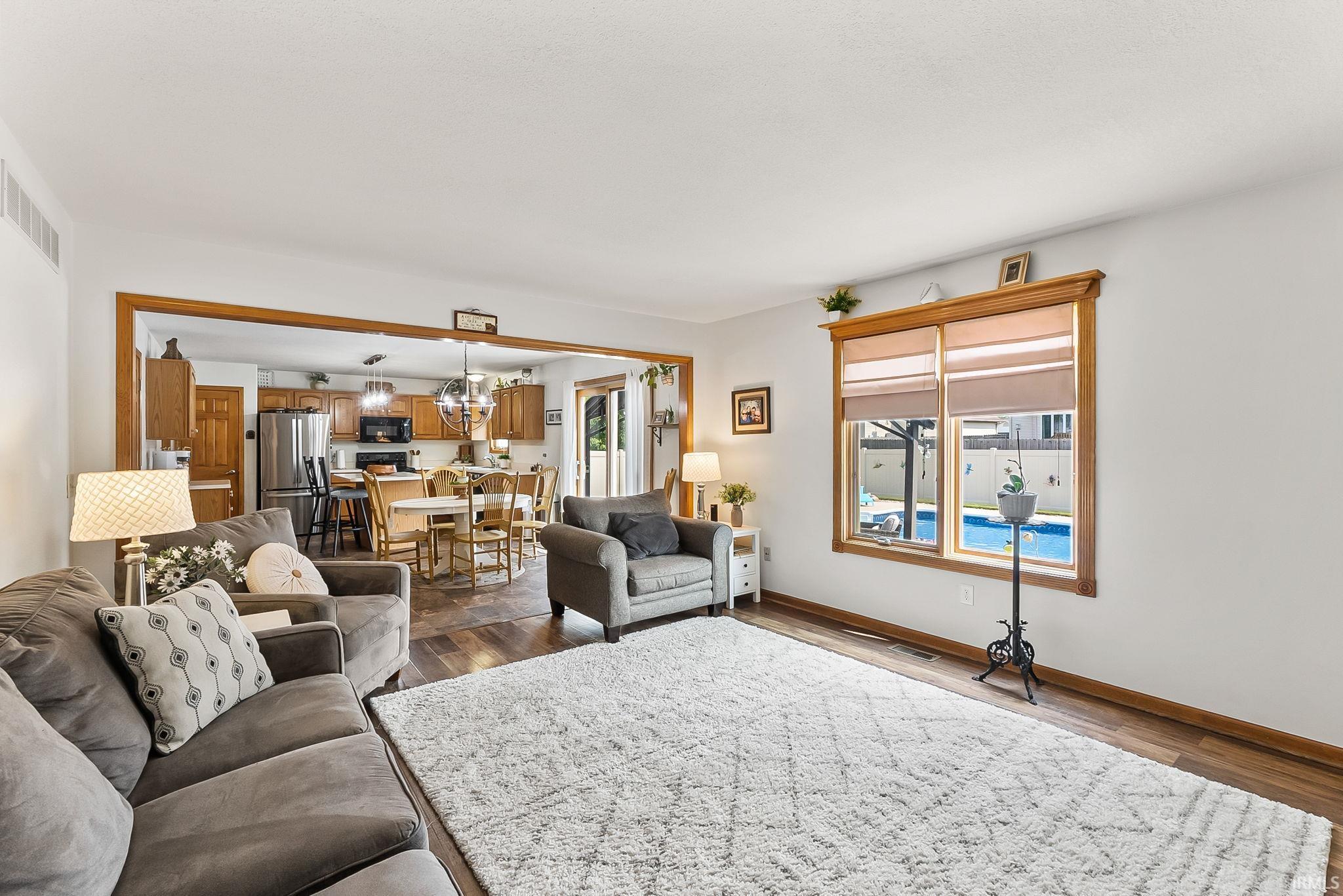 Living area featuring wood-finish flooring, a large window with pool visibility, and an open doorway to the kitchen
