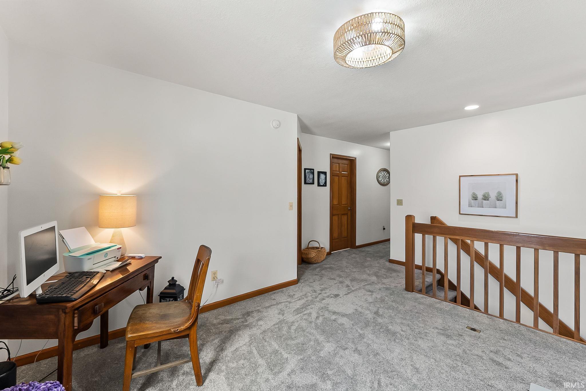 Spacious upper-level landing featuring light gray carpeting, white walls, and warm wood-tone trim