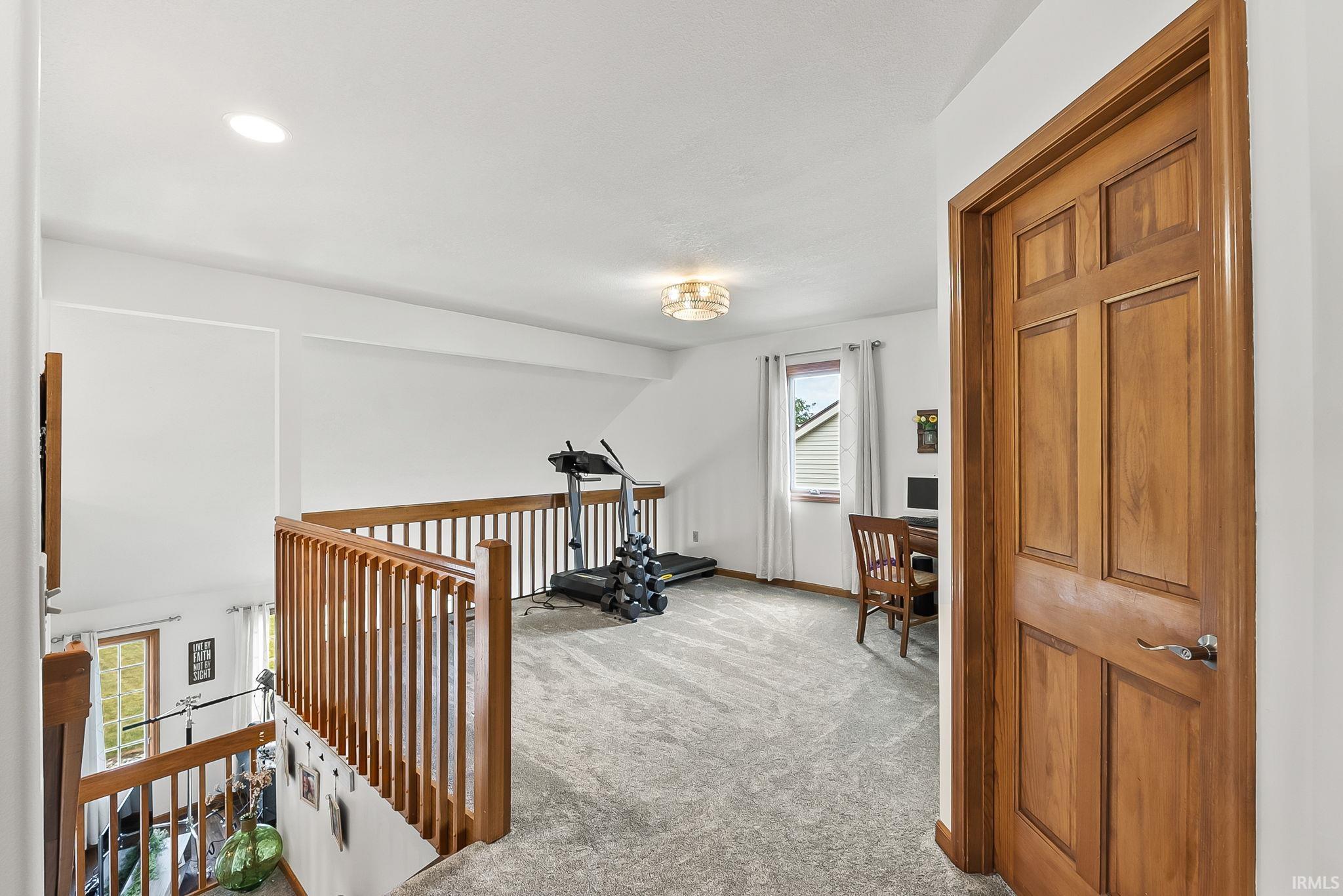 Carpeted loft area with wood banister, recessed lighting, and a window