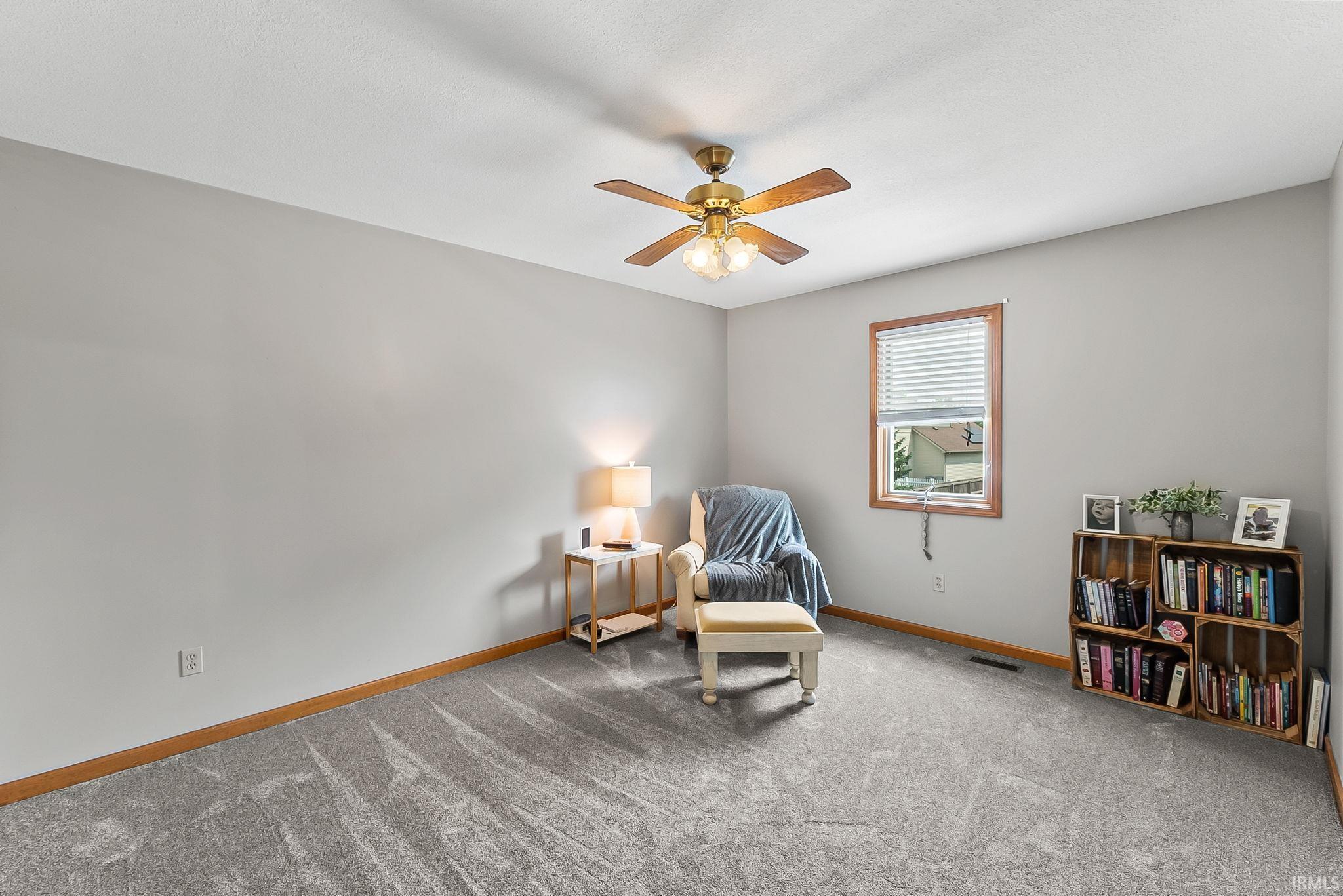 Carpeted room featuring a ceiling fan with integrated lighting, neutral wall tones, a wood-trimmed window with blinds, and wood baseboards