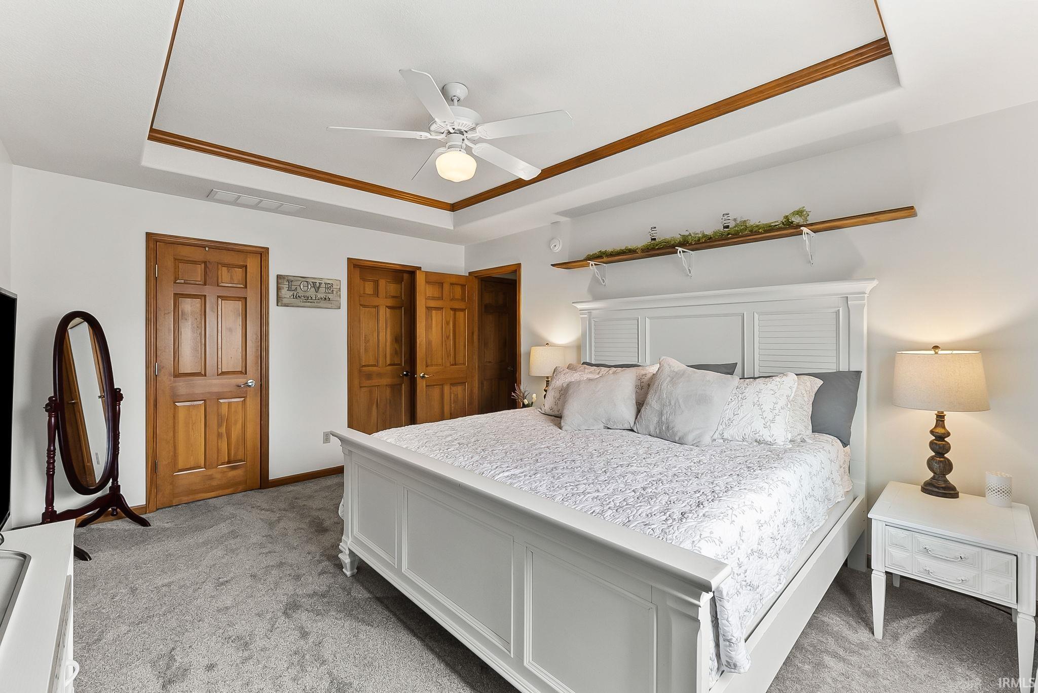 Tray ceiling featuring wood-finish trim, ceiling fan with integrated lighting, two wood-paneled doors, and gray carpet flooring