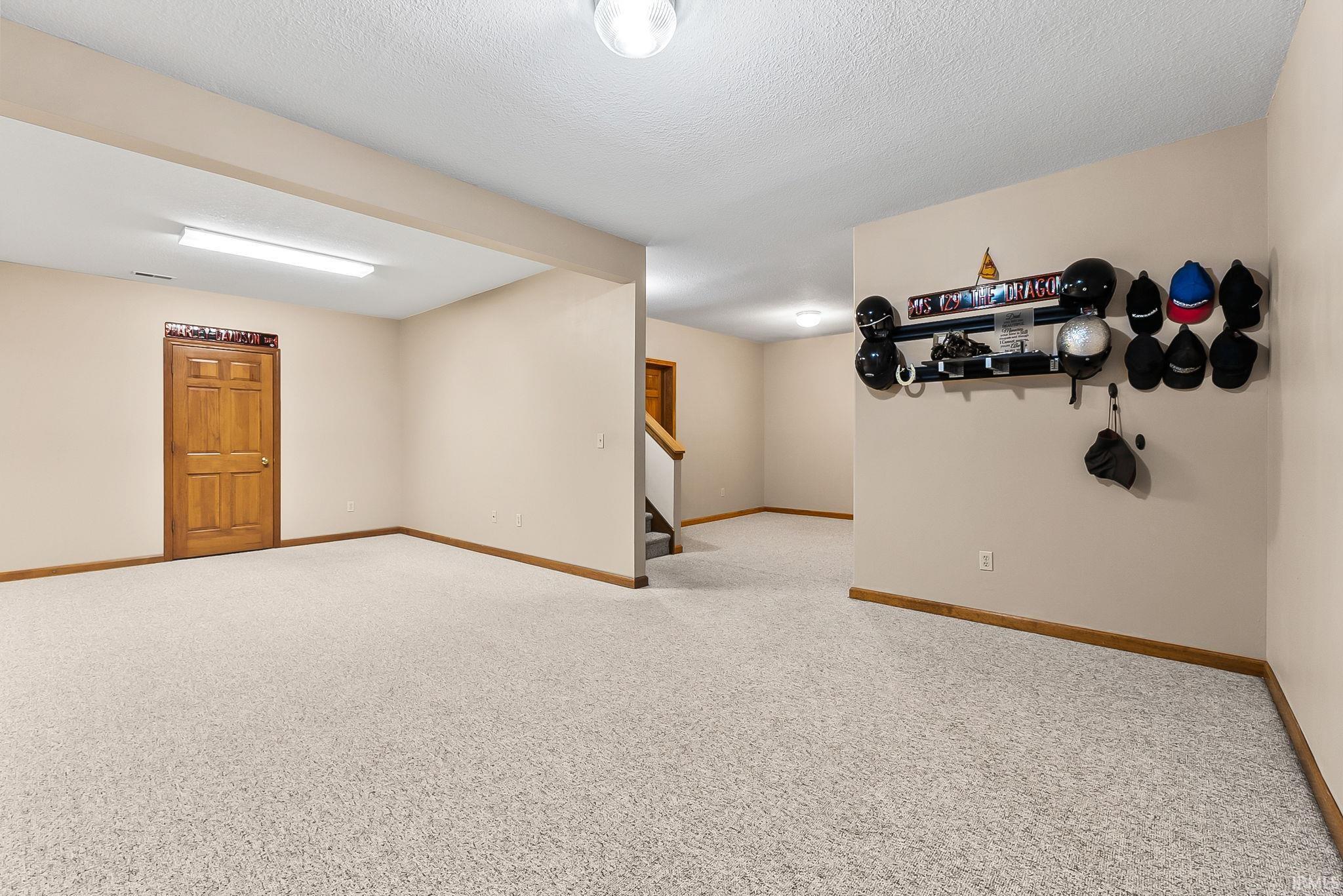 Spacious room with light-toned walls, neutral carpet flooring, and wood-finish trim
