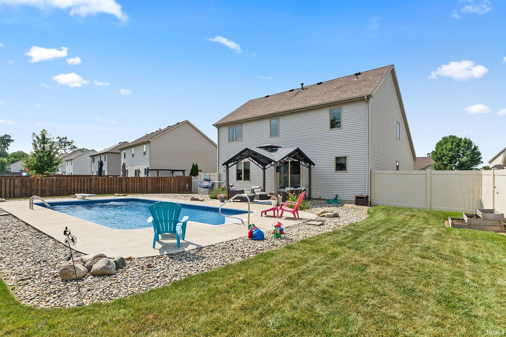 Backyard featuring an in-ground swimming pool with concrete surround, a covered patio area, and a tiered garden bed