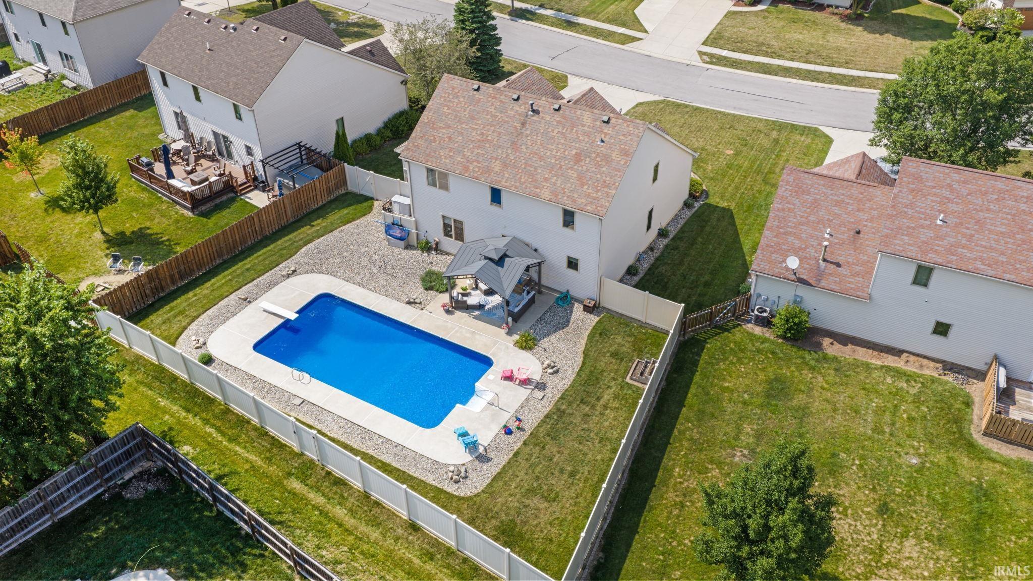 Fenced backyard featuring an in-ground swimming pool with diving board, a patio area with a gazebo, and surrounding gravel landscaping