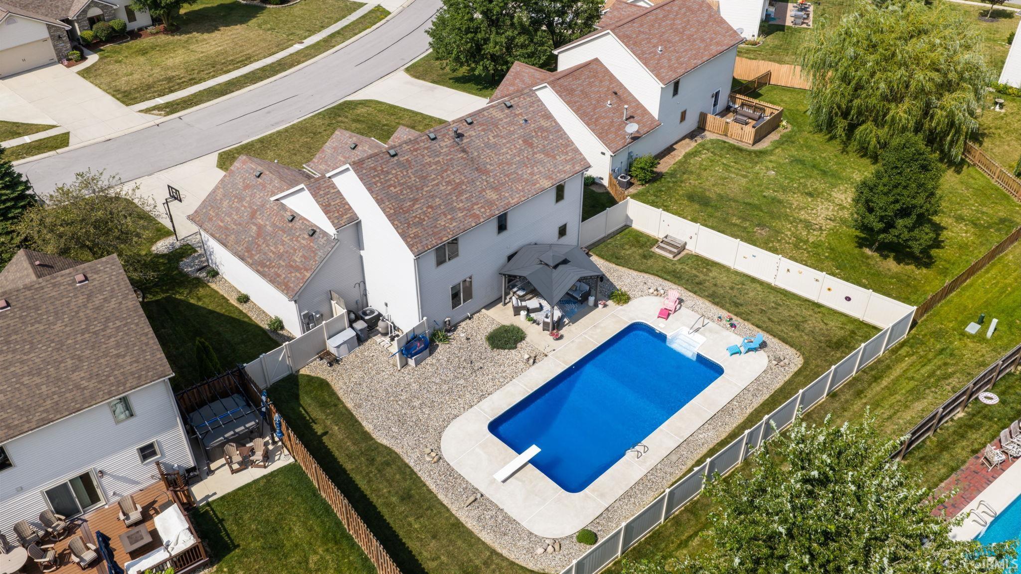 Expansive backyard featuring an in-ground swimming pool with diving board, surrounded by a concrete patio and decorative rock landscaping