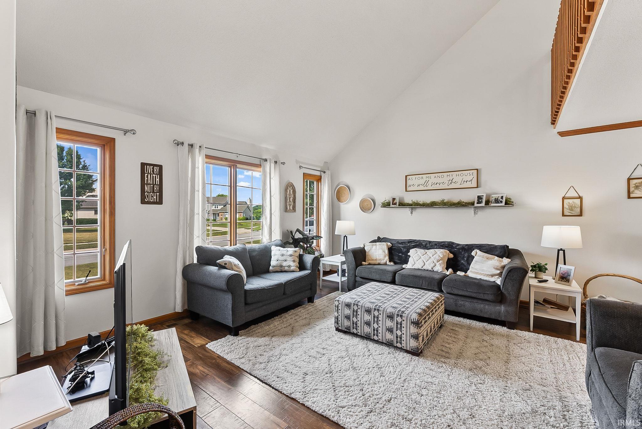 Living area featuring wood-finish flooring, a vaulted ceiling, and multiple windows with wood trim