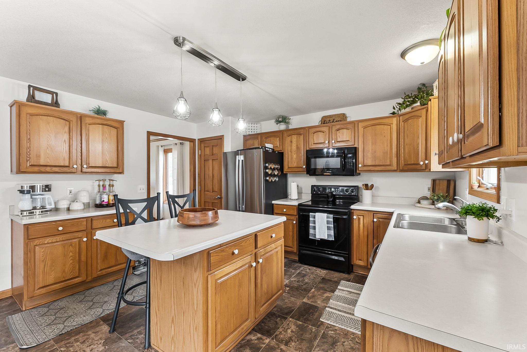 Kitchen featuring a central island with a white countertop, wood-finish cabinetry, stainless steel sink, black range, and stainless steel refrigerator
