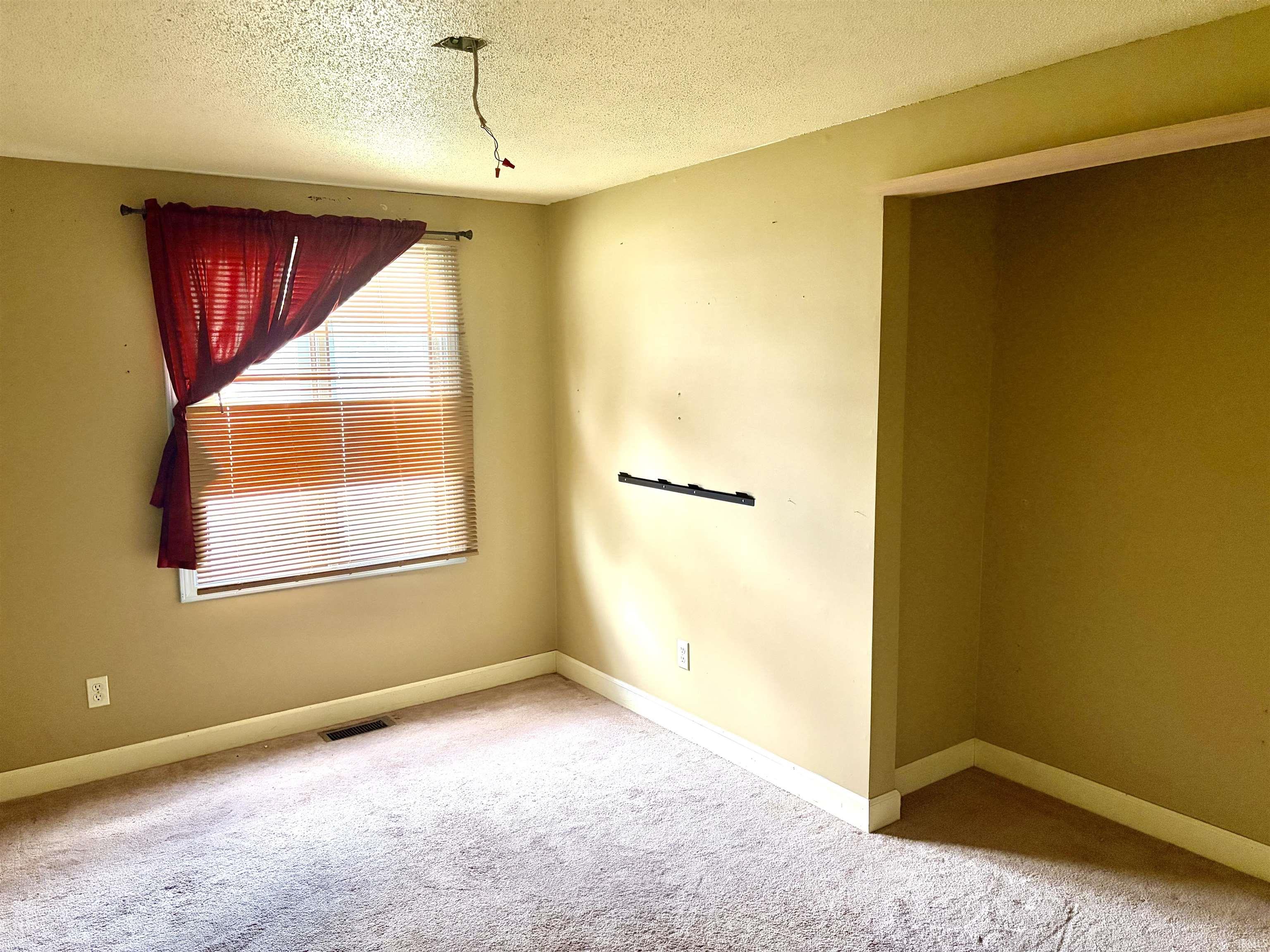 Carpeted room with a window featuring blinds and a curtain rod