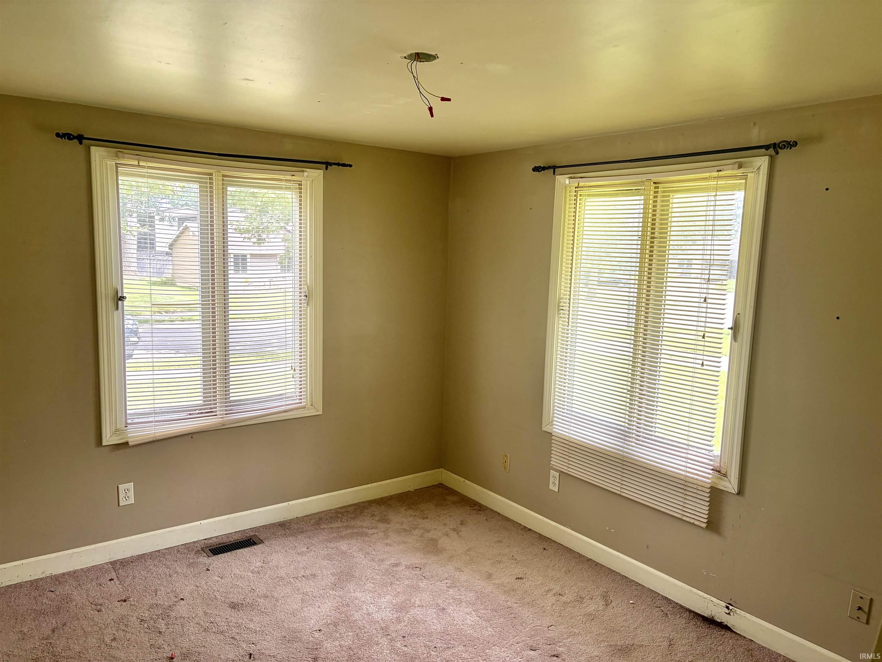 Room featuring two windows with horizontal blinds, tan walls, white trim, and carpeted flooring