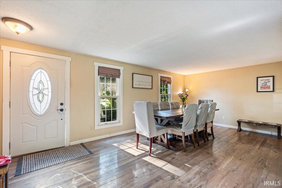 Spacious room featuring wood-finish flooring, a decorative front entry door with an oval glass insert, and two windows with Roman shades