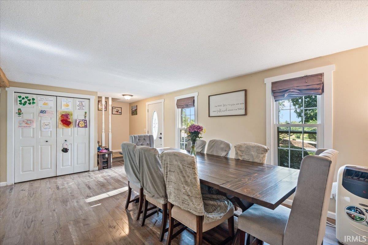 Open-concept dining area featuring wood-finish flooring, two large windows with valance treatments, and a white entrance door with decorative glass