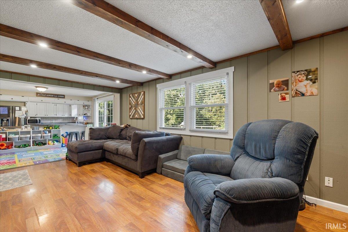 Living area featuring wood-finish flooring, exposed ceiling beams with recessed lighting, and paneling on walls