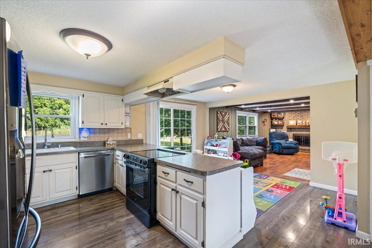 Kitchen with wood-finish flooring, white cabinetry, a central island, and stainless steel appliances, including a dishwasher and refrigerator