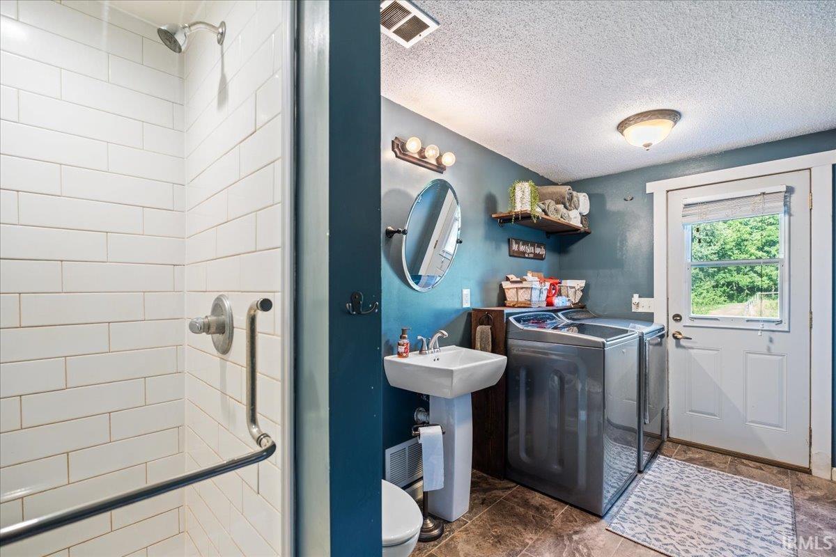 Combination bathroom and laundry area featuring a tiled shower stall with a grab bar, a pedestal sink, and dedicated space for laundry appliances