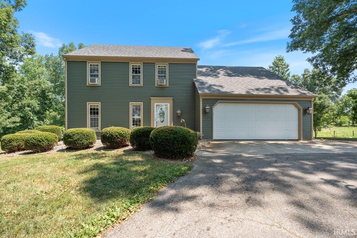 Two-story residence featuring green siding, a shingled roof, and a two-car garage with overhead door