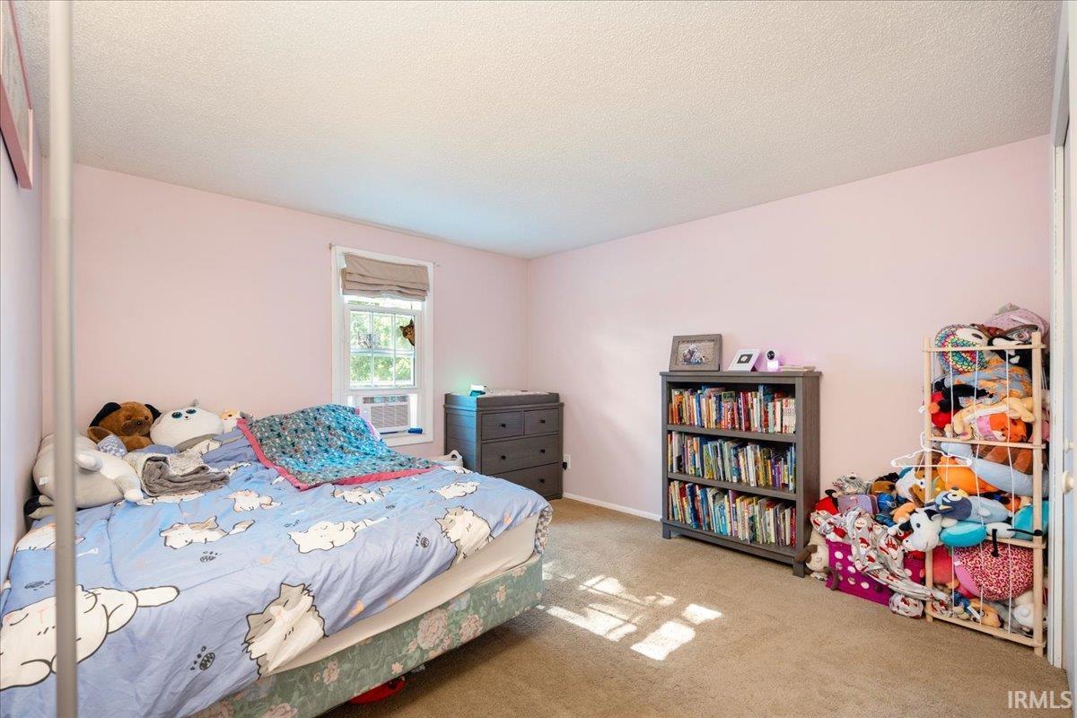 Bedroom featuring a window with a Roman shade, light pink walls, and neutral carpet