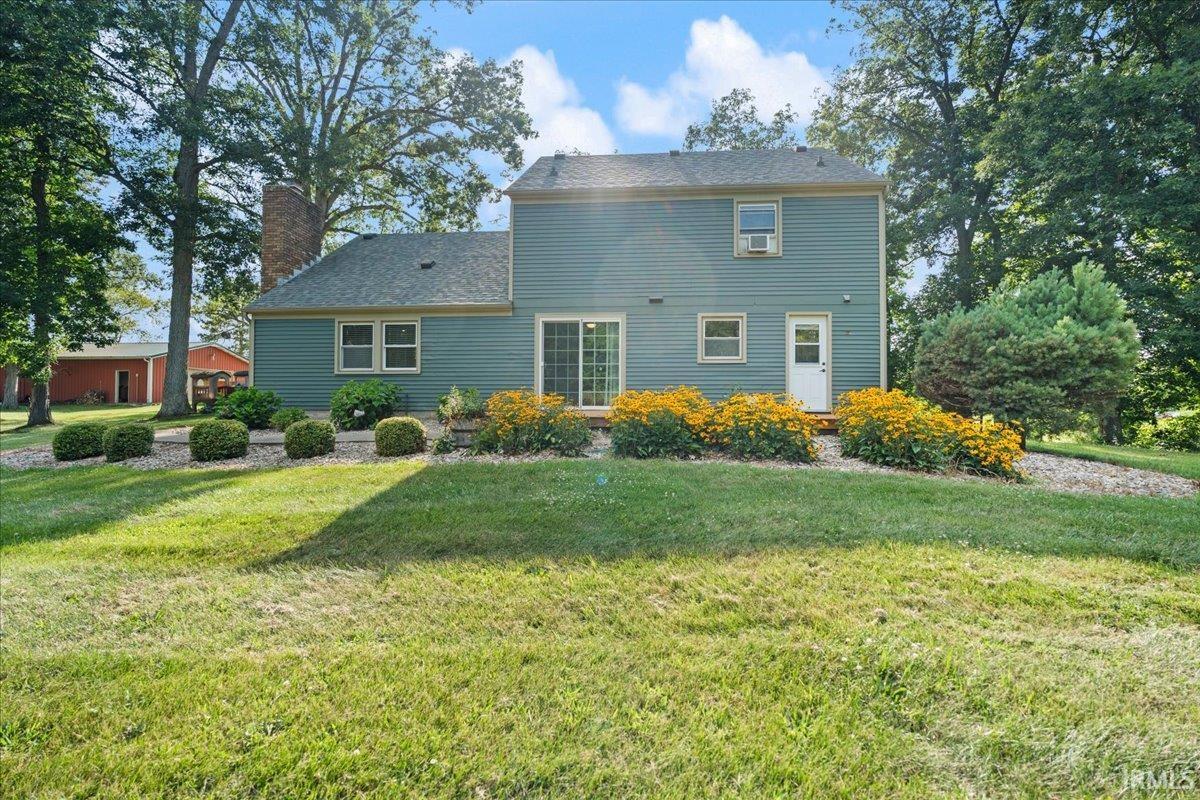 Expansive backyard featuring a manicured lawn, established landscaping, mature trees, and a red outbuilding