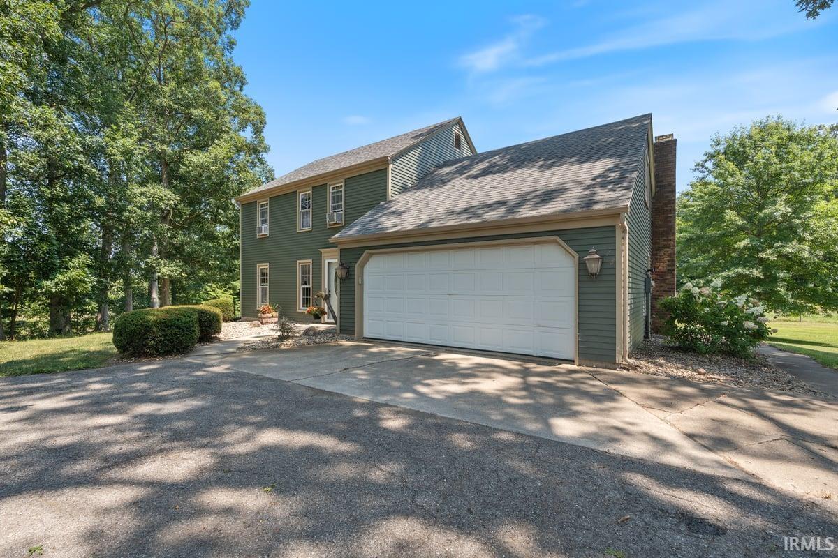Two-story residence featuring green siding, a dual-bay garage with a white door, and a prominent brick chimney