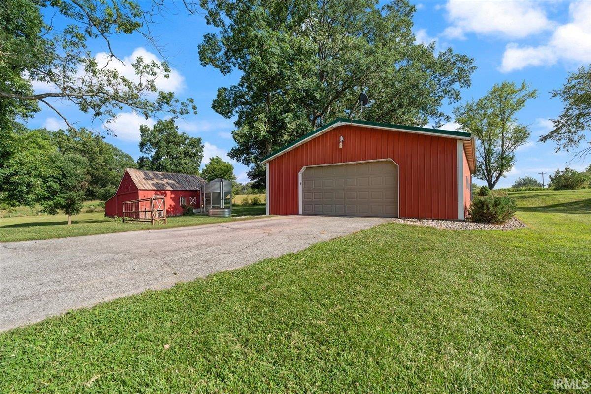 Red metal outbuilding with a green roof, featuring a large garage door and gravel landscaping