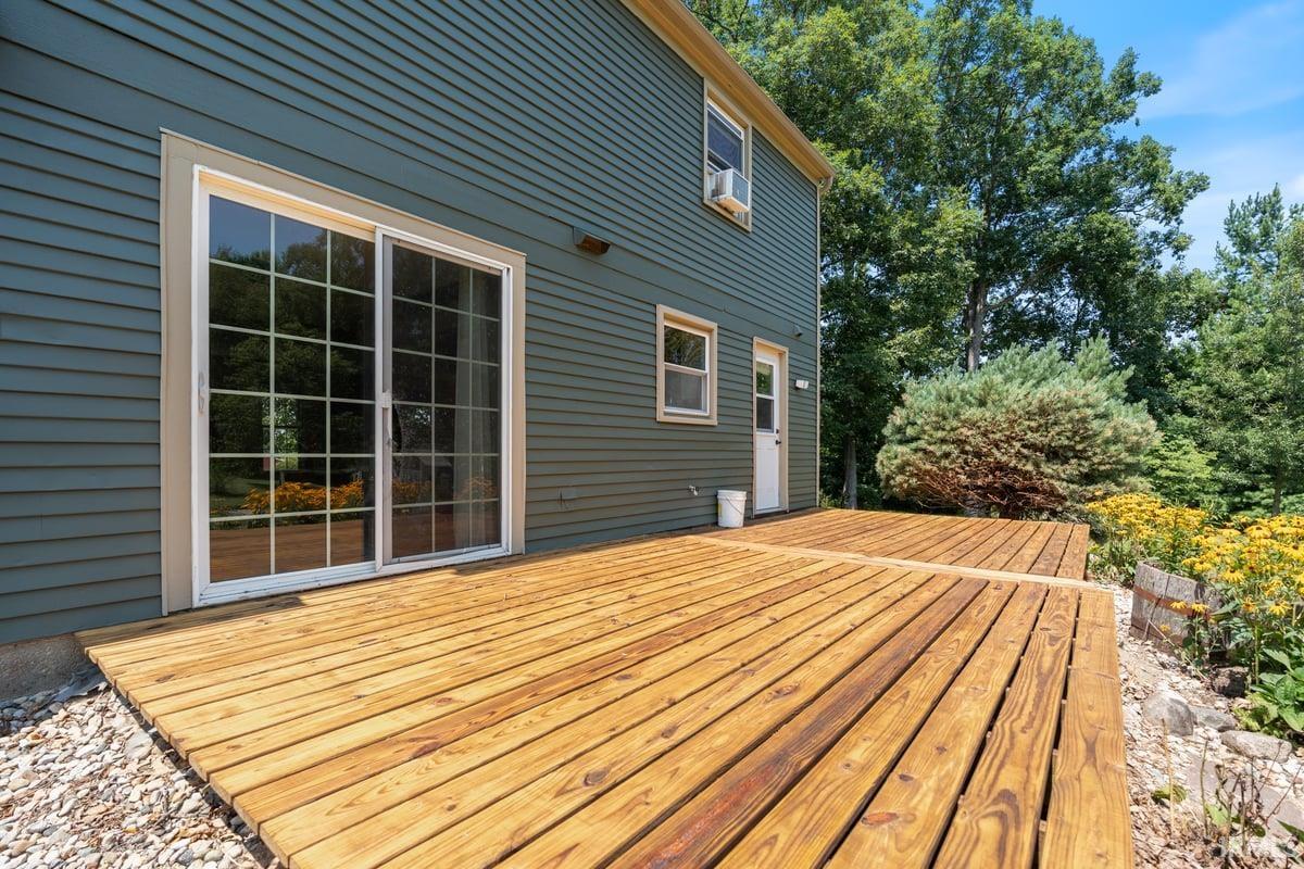 Expansive wood deck with a natural finish, featuring a sliding glass door with grid patterns and a backdrop of mature trees