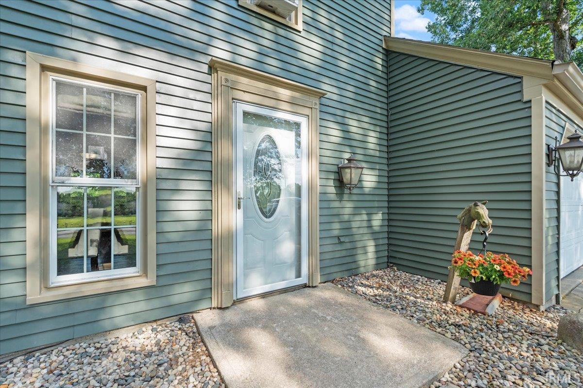 Exterior entry featuring horizontal siding, a white storm door with decorative glass, and a concrete walkway