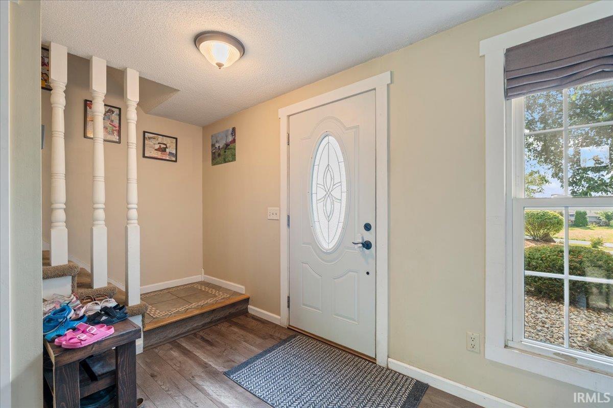 Entryway featuring wood-finish flooring, a white front door with an oval decorative glass insert, and a double-pane window with white trim