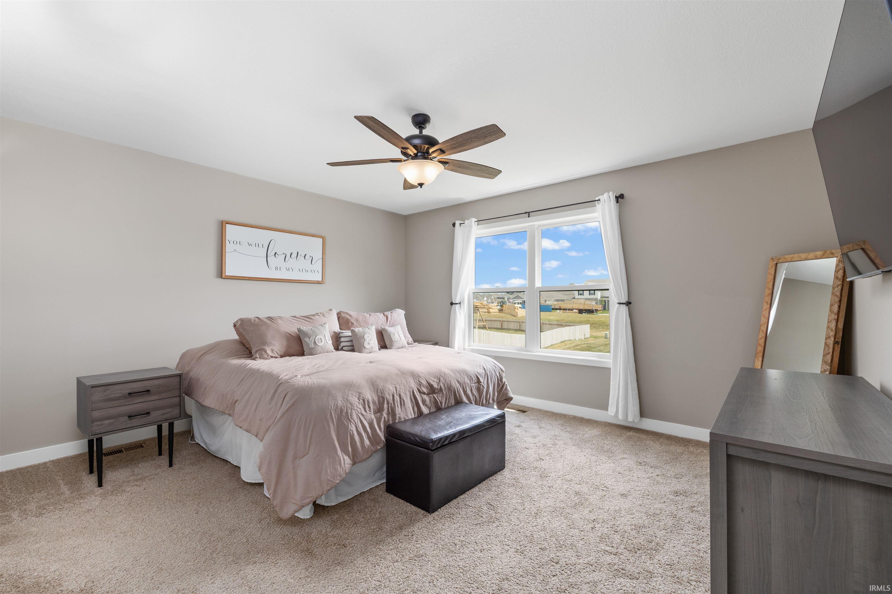 Carpeted sleeping area with a large window, a ceiling fan with integrated lighting, and neutral wall tones