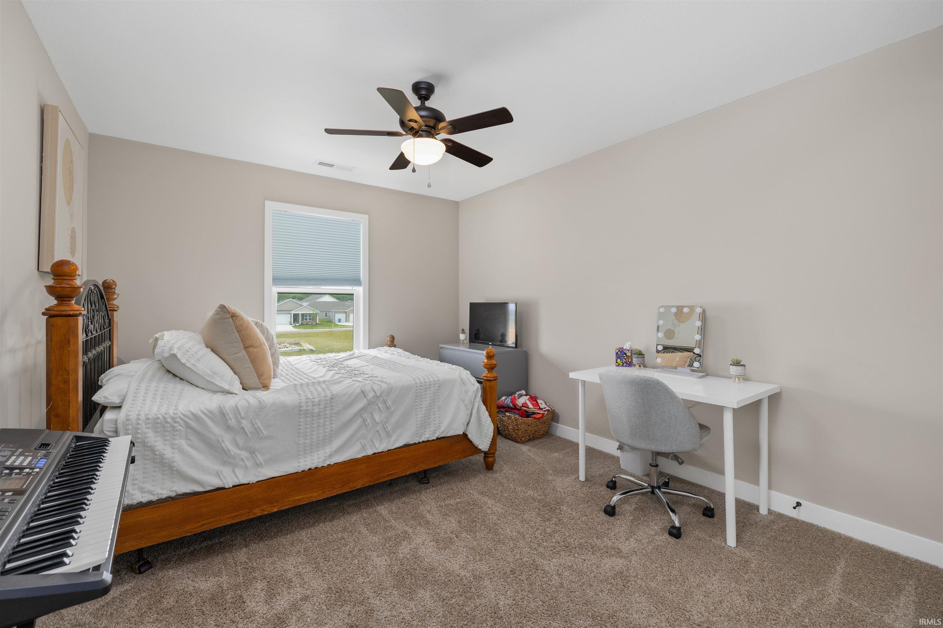 Carpeted bedroom featuring neutral wall tones, a single window with a roller blind, and a ceiling fan with integrated lighting