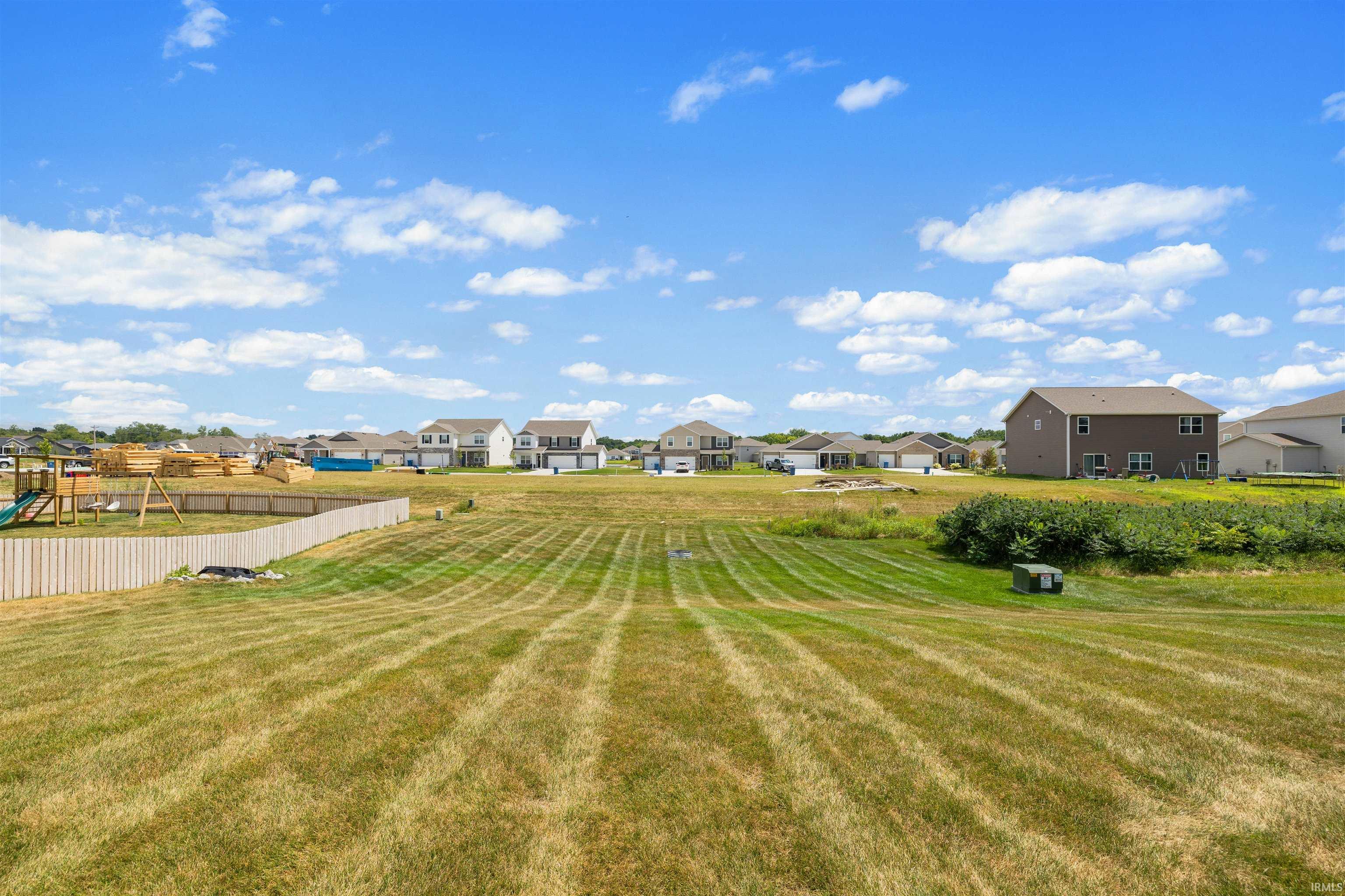 Expansive backyard featuring a large grassy area, a partial wood privacy fence, and mature green foliage