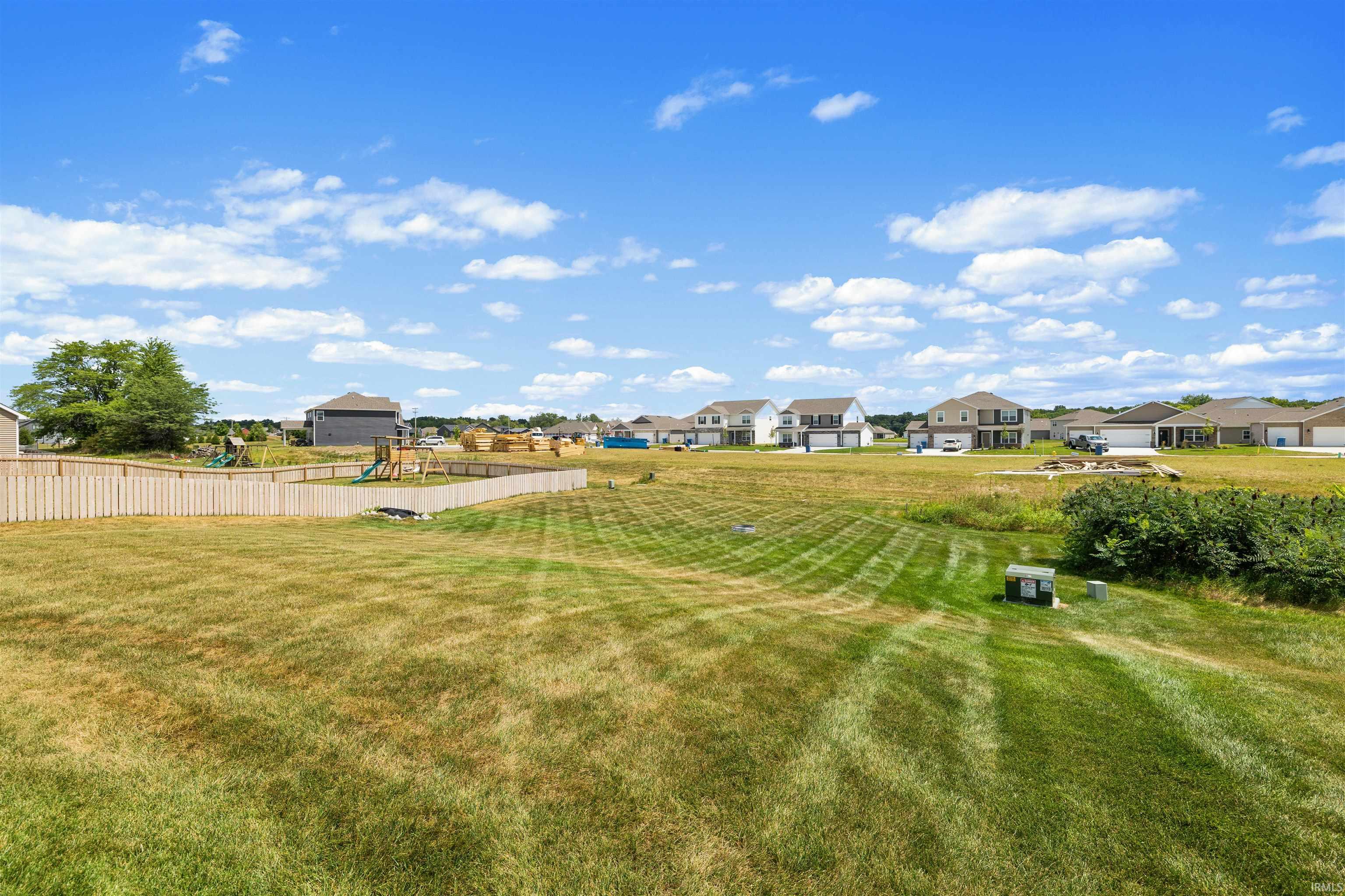 Expansive green space featuring a wooden privacy fence, natural foliage, and distant residential structures