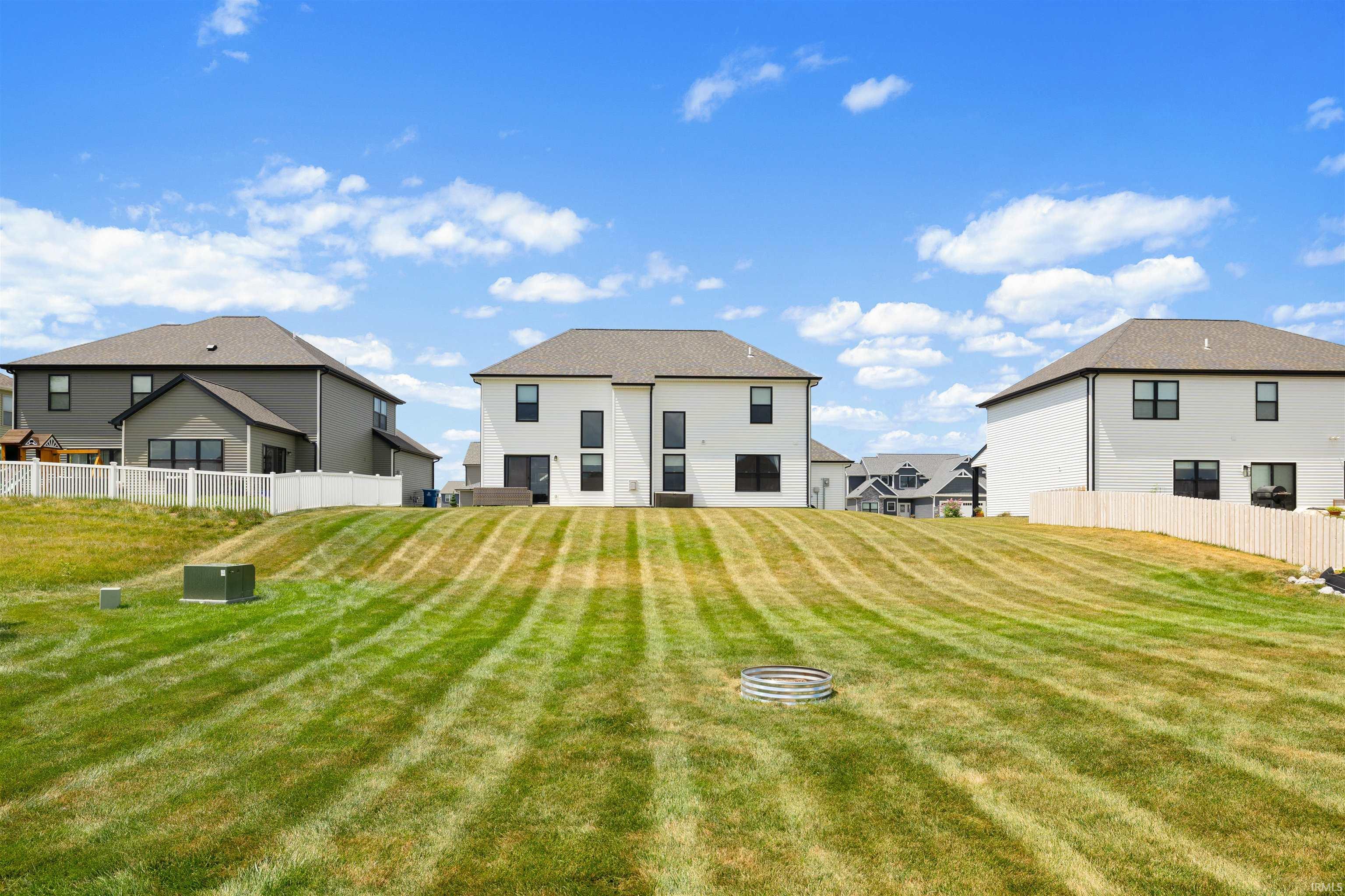 Rear exterior featuring a white facade with black-framed windows, a walk-out patio, and a sloped lawn