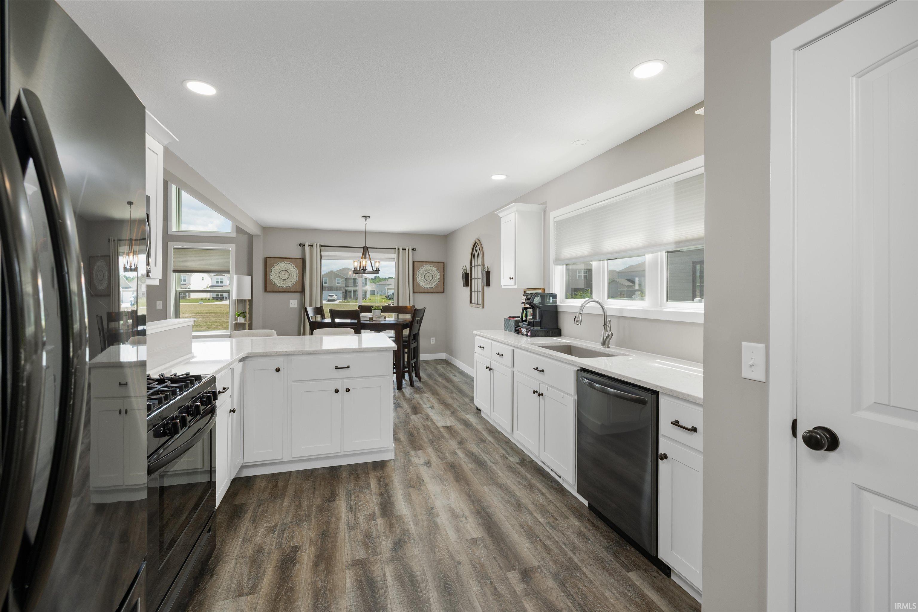 Modern kitchen featuring white cabinetry, light-toned countertops, stainless steel appliances, and wood-finish flooring