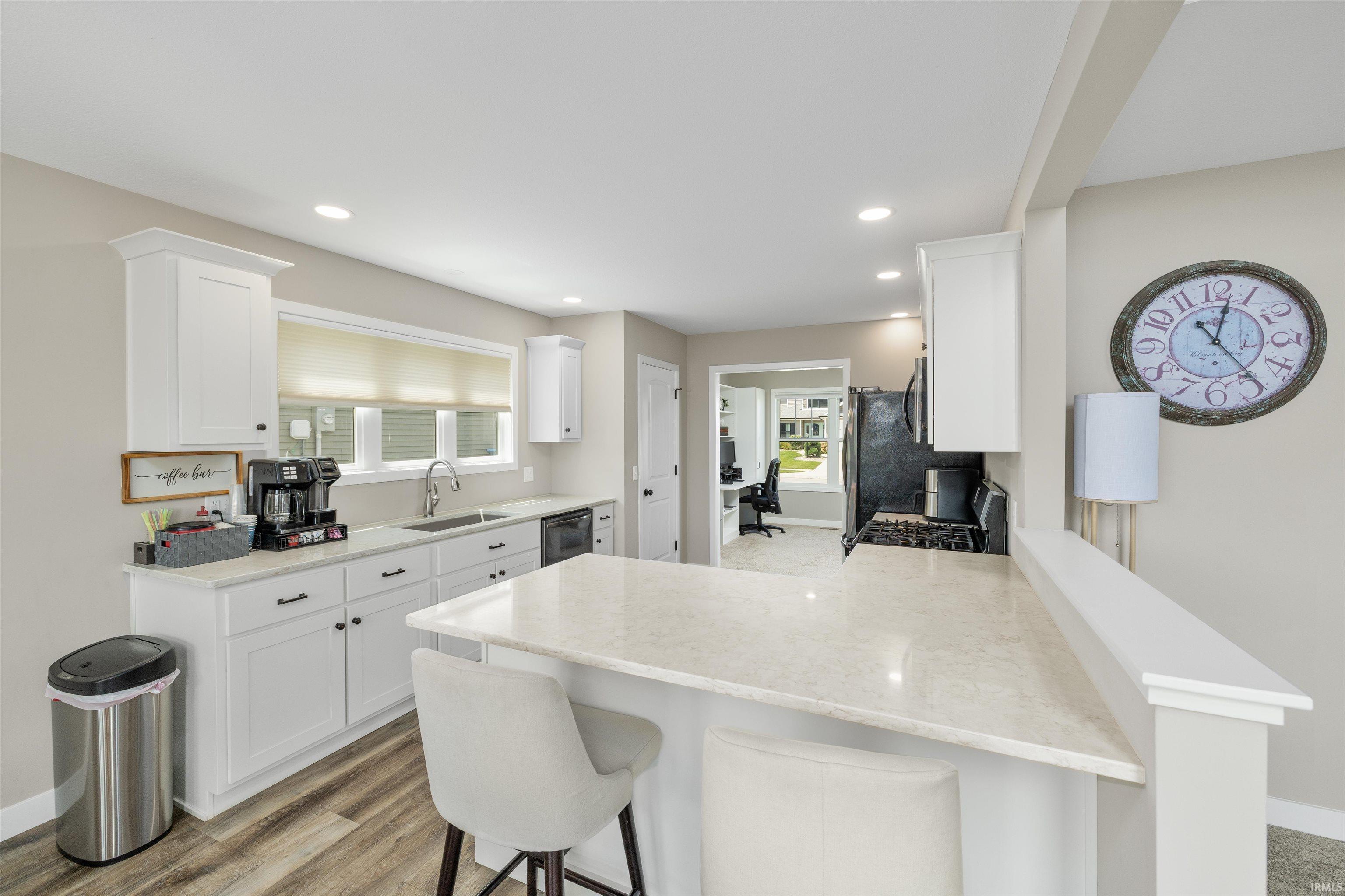 Kitchen featuring an island with stone countertops, white shaker cabinetry, recessed lighting, wood-finish flooring, and a stainless steel sink with a gooseneck faucet