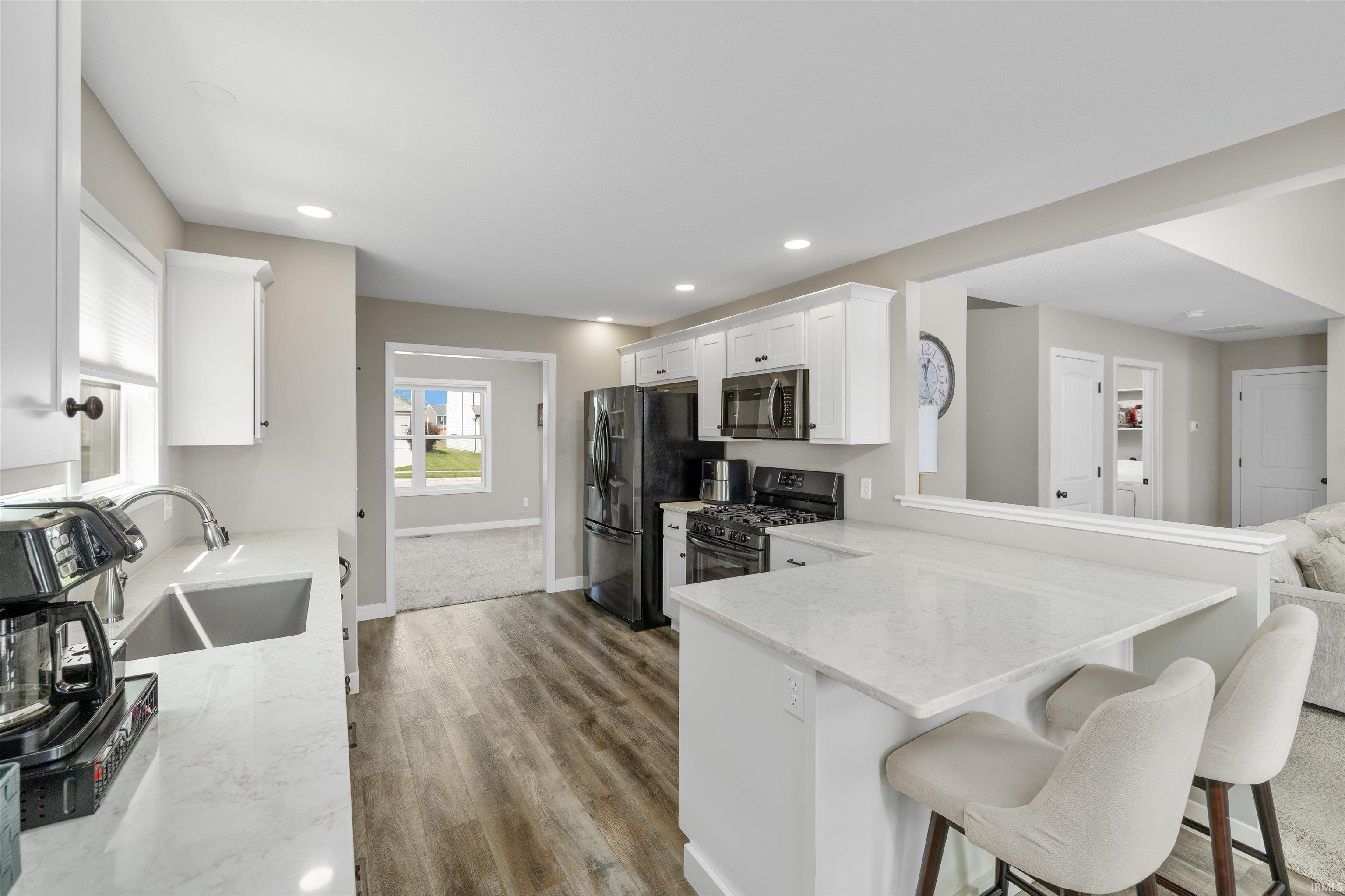Kitchen featuring white cabinetry, light-toned countertops, a stainless steel sink, and wood-finish flooring