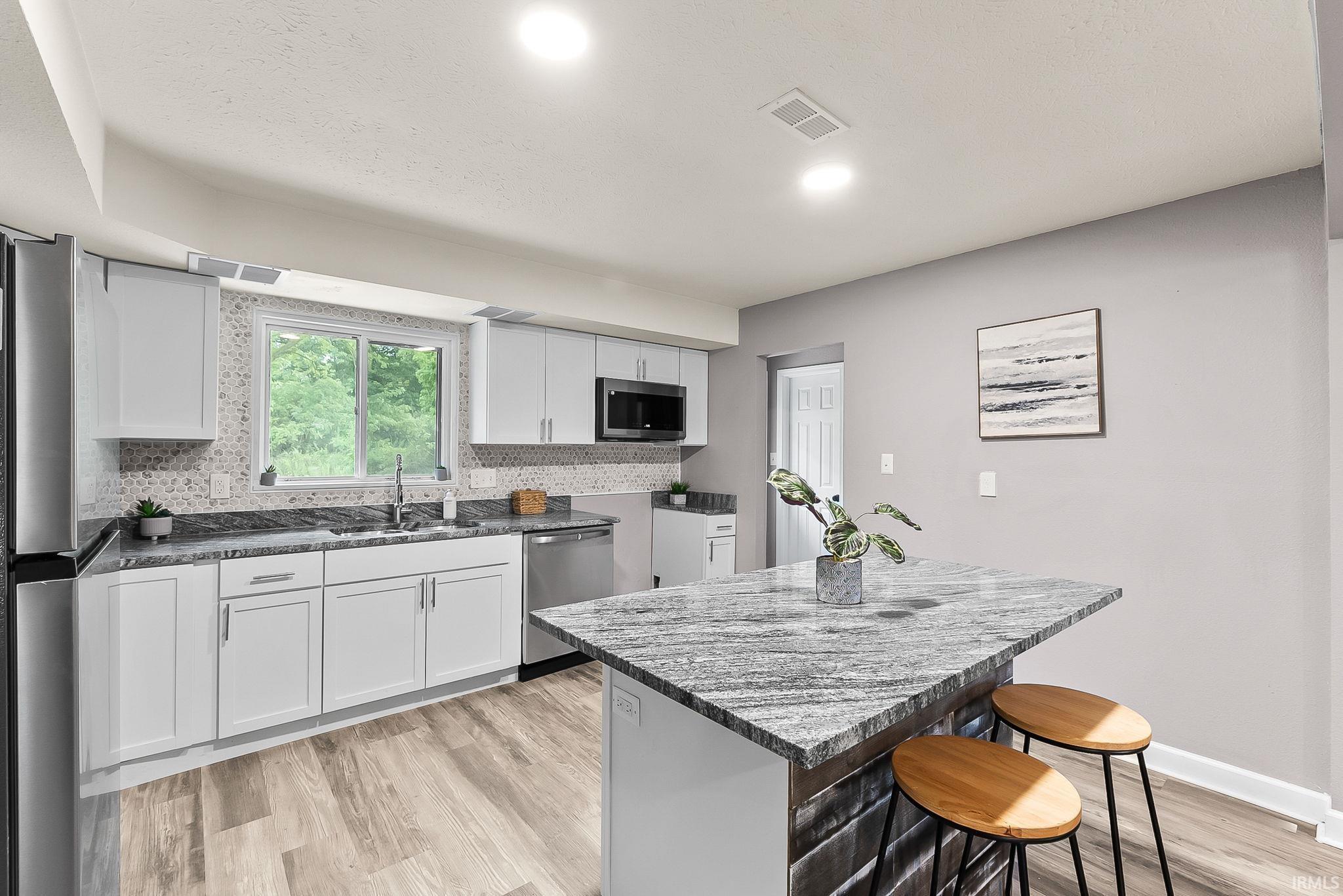Kitchen featuring white cabinetry, stainless steel appliances, a mosaic tile backsplash, and wood-finish flooring