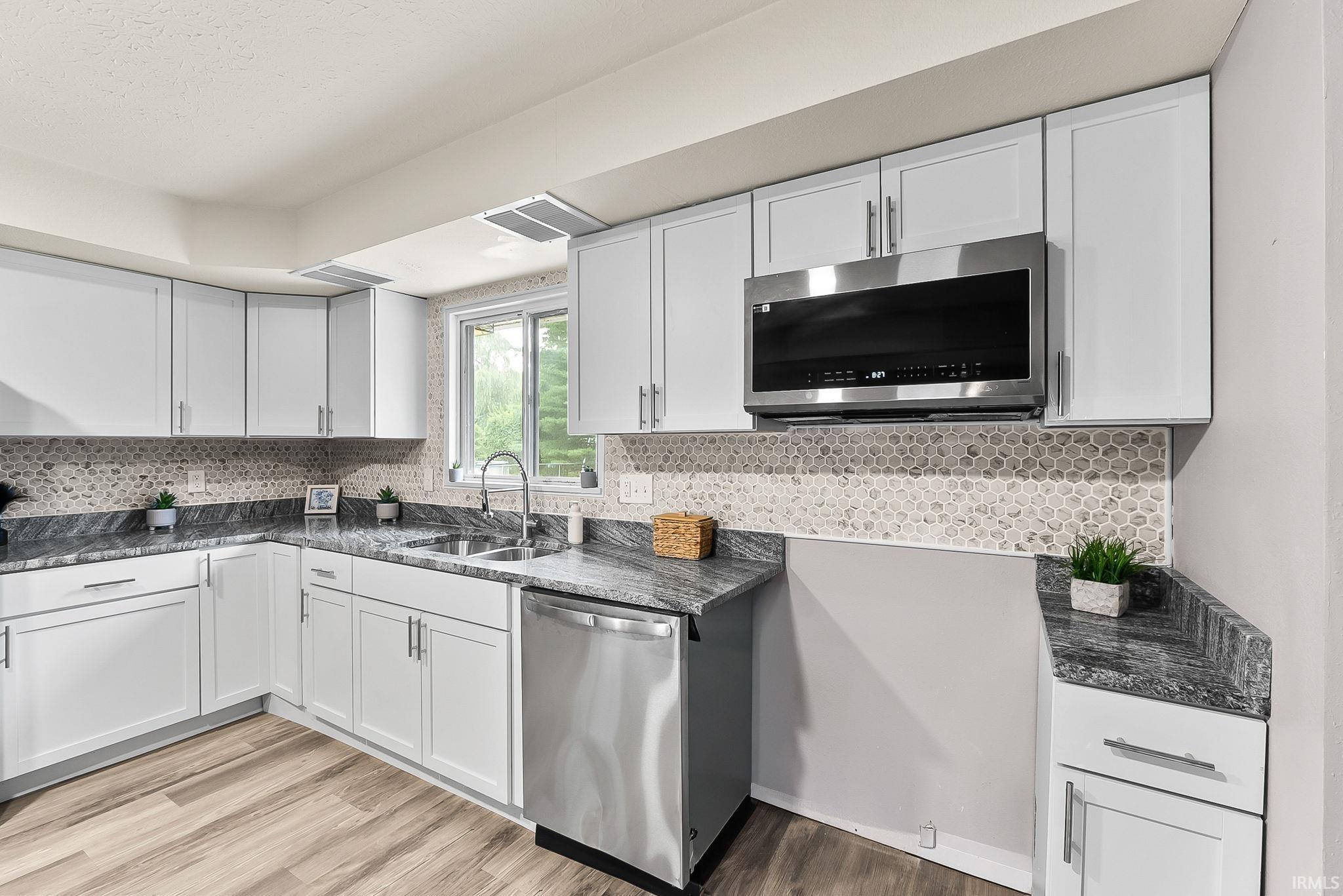 Modern kitchen featuring white cabinetry, dark stone countertops, a mosaic tile backsplash, stainless steel appliances, and wood-finish flooring