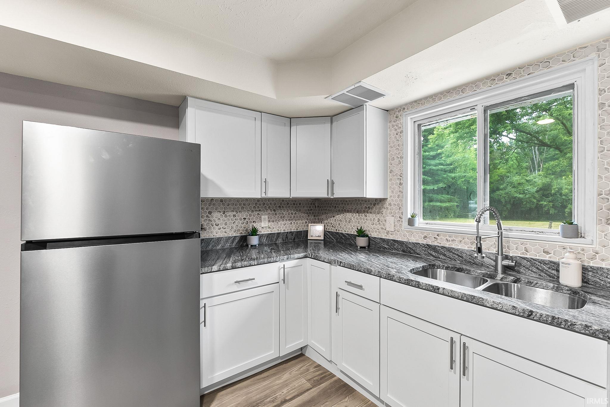 Modern kitchen featuring white cabinetry, a stainless steel refrigerator, stone countertops, and a double basin sink with a gooseneck faucet
