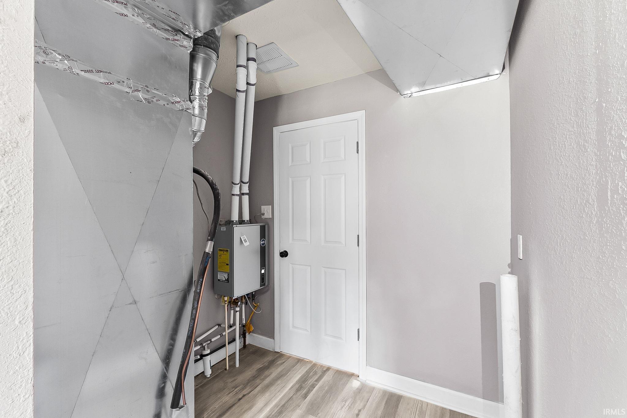 Utility area with a tankless water heater, exposed ductwork, and wood-finish flooring