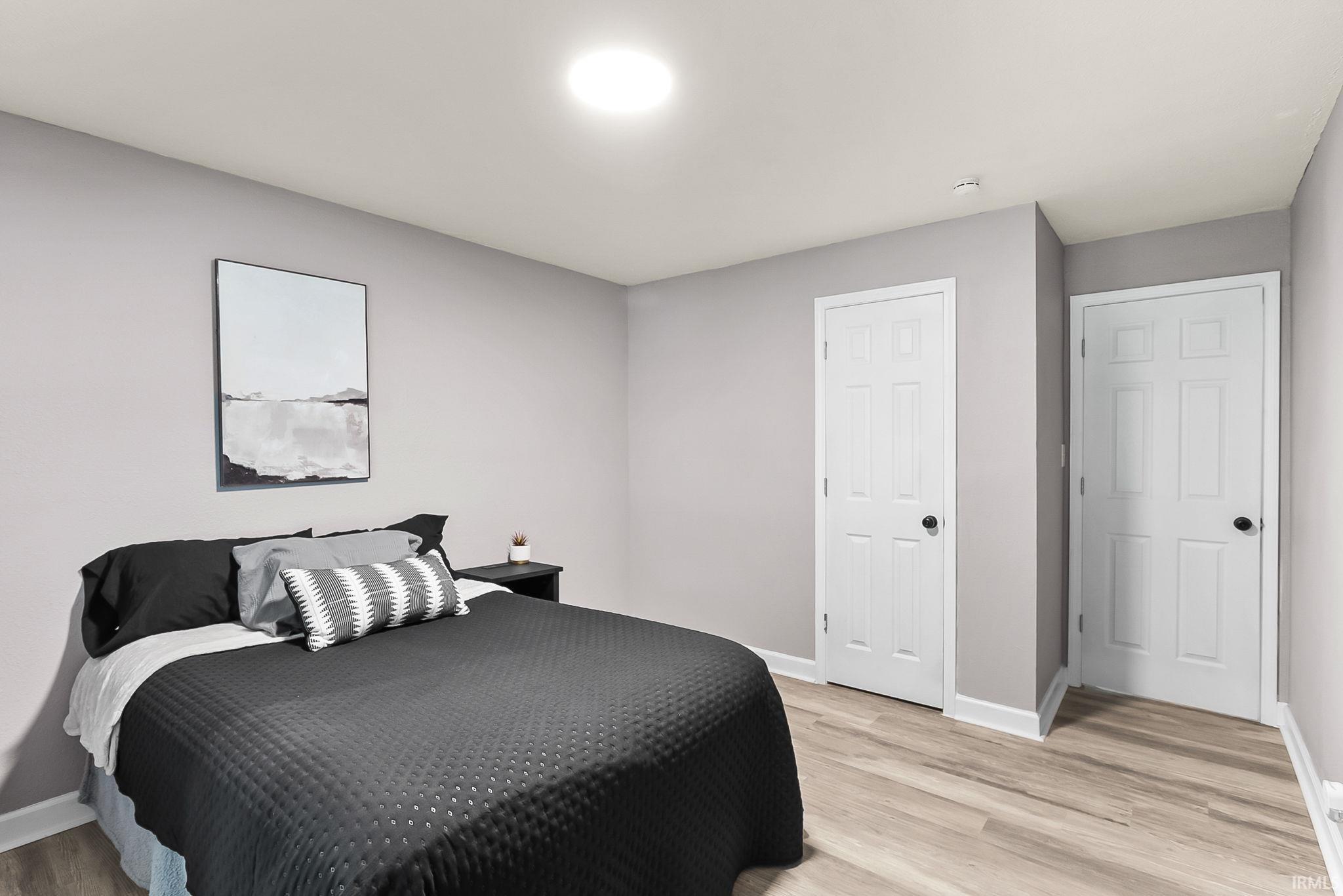 Neutral-toned room featuring light wood-finish flooring, a contemporary flush-mount ceiling light, white baseboards, and two white paneled doors with dark hardware